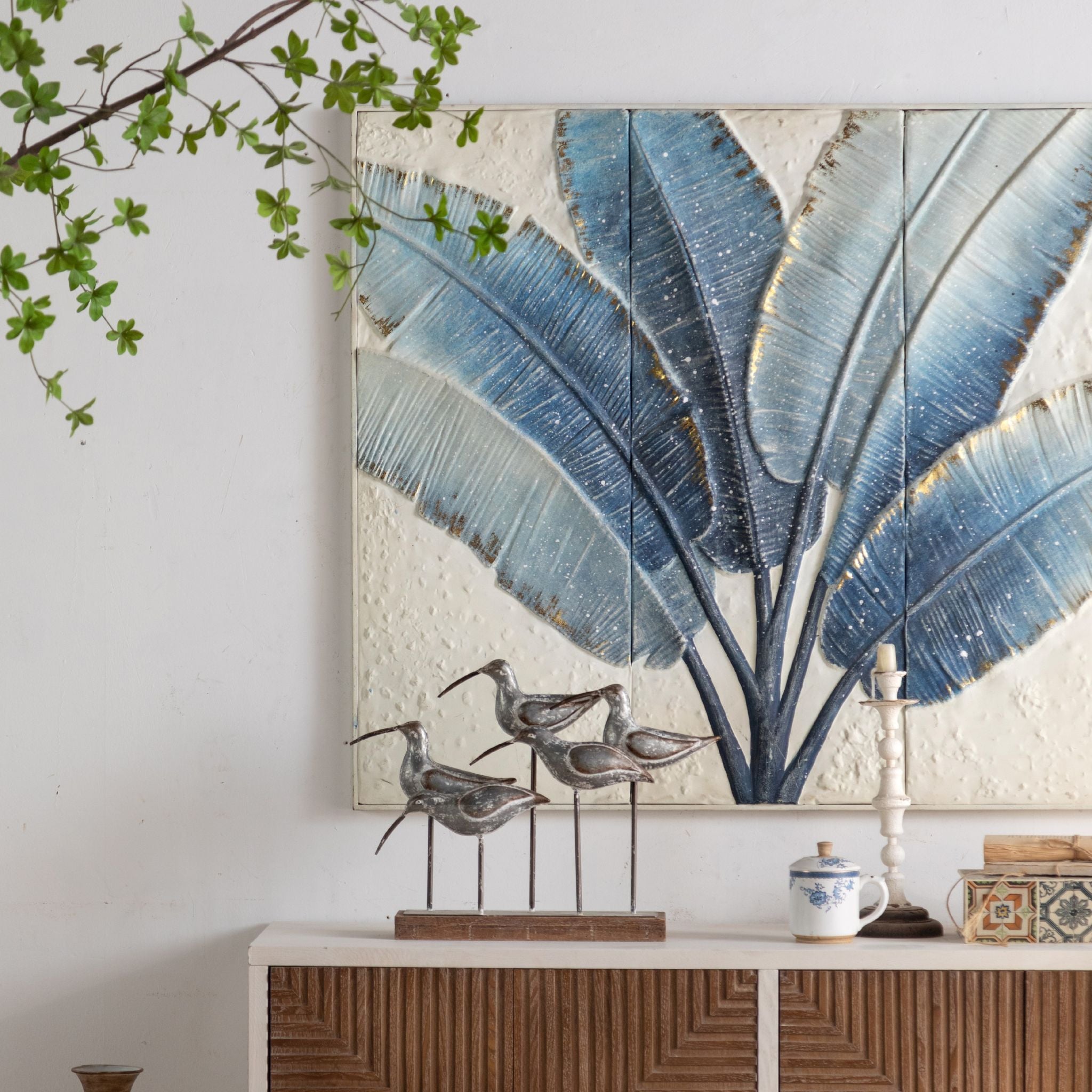 Tino blue leaf embossed wall art in a living room above a sideboard with vases