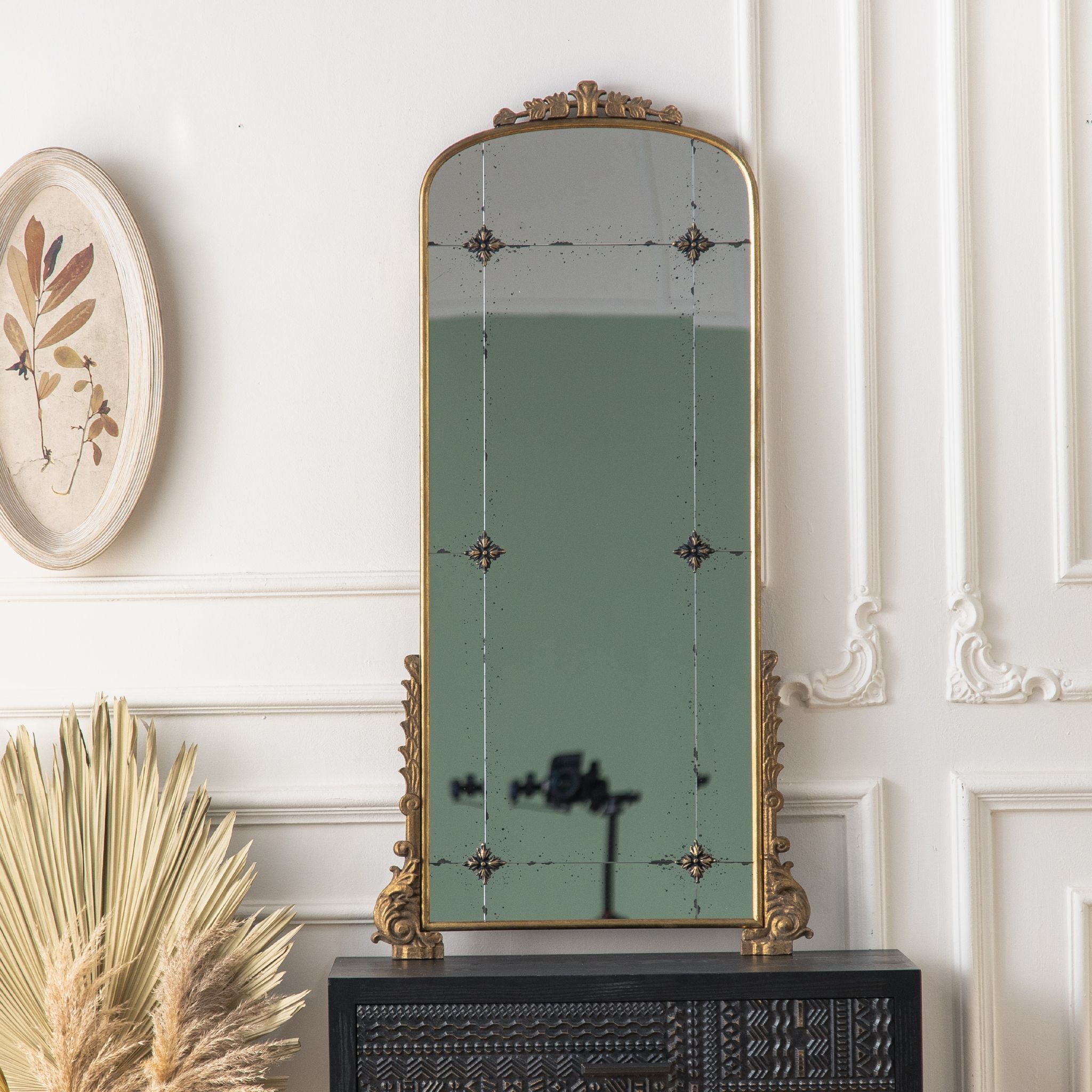 Thea arched mirror in aged gold with antiqued panelled glass standing above a console