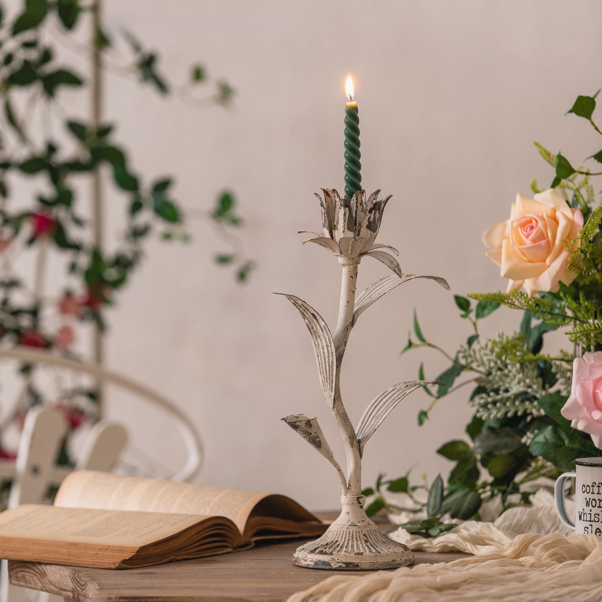 Siena flower candle holder in distressed white iron with a green taper candle on a table