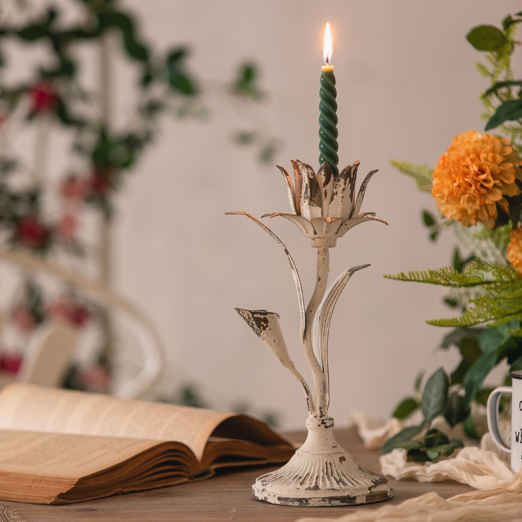 Silvio flower candle holder in distressed white iron with a green taper candle on a table