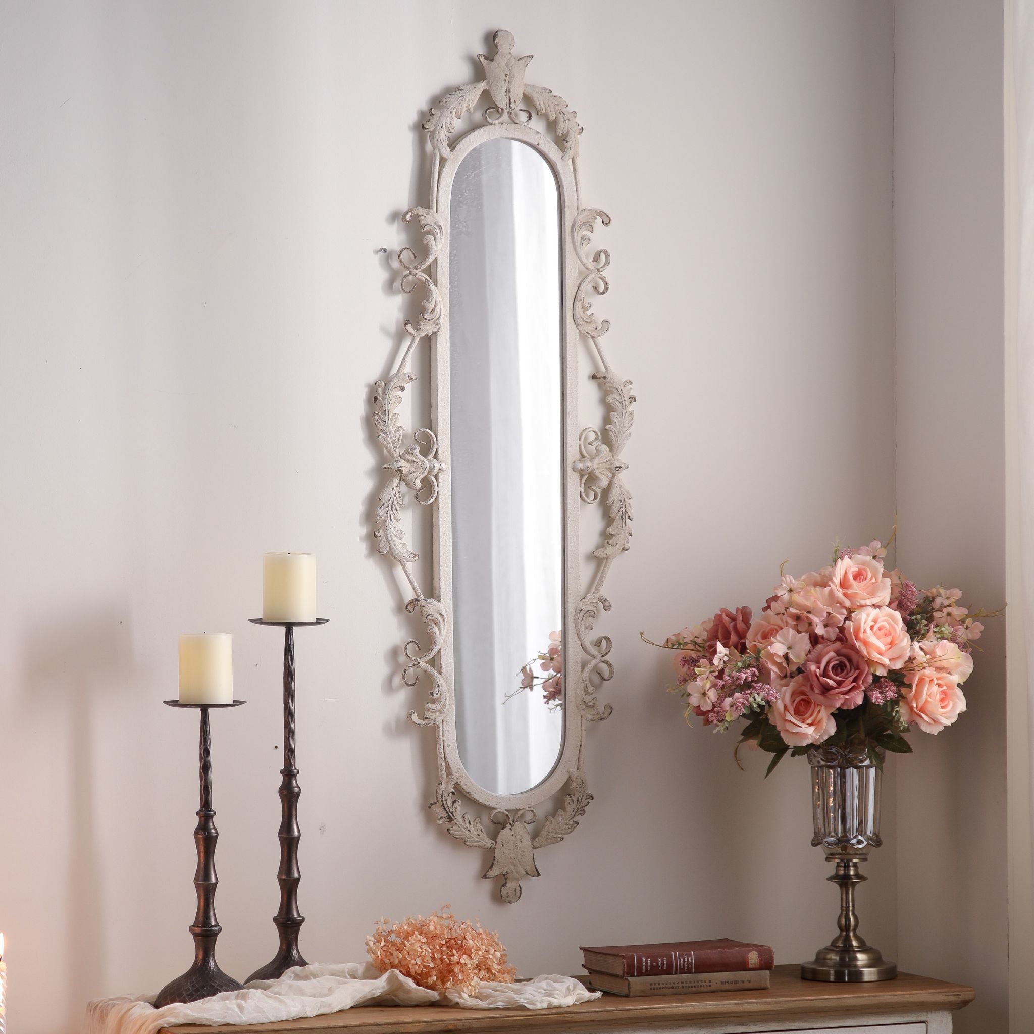 Pilar mirror styled on a wall with candlesticks and pink roses on a sideboard