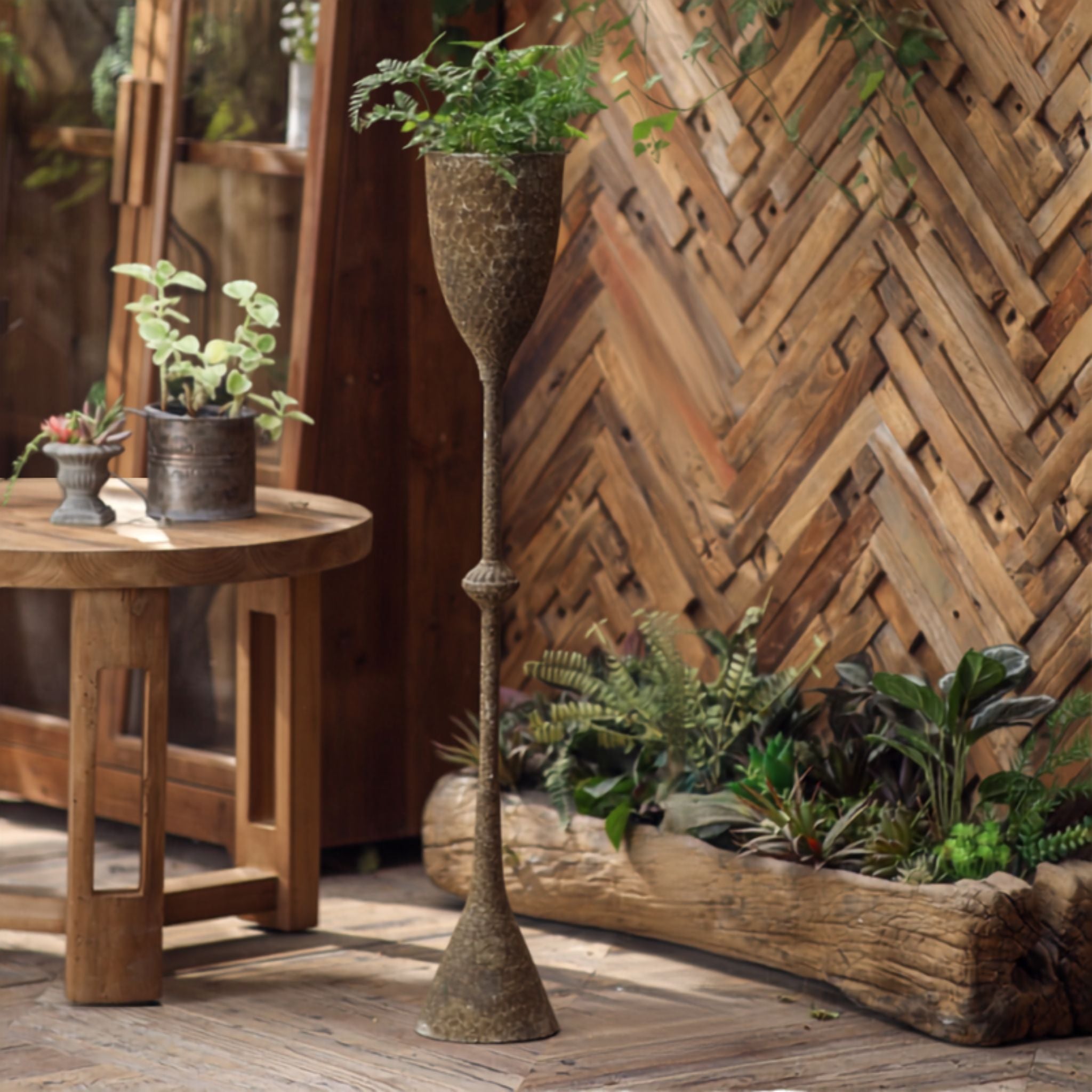Greta tall goblet planter in aged iron with a fern beside a herringbone timber wall