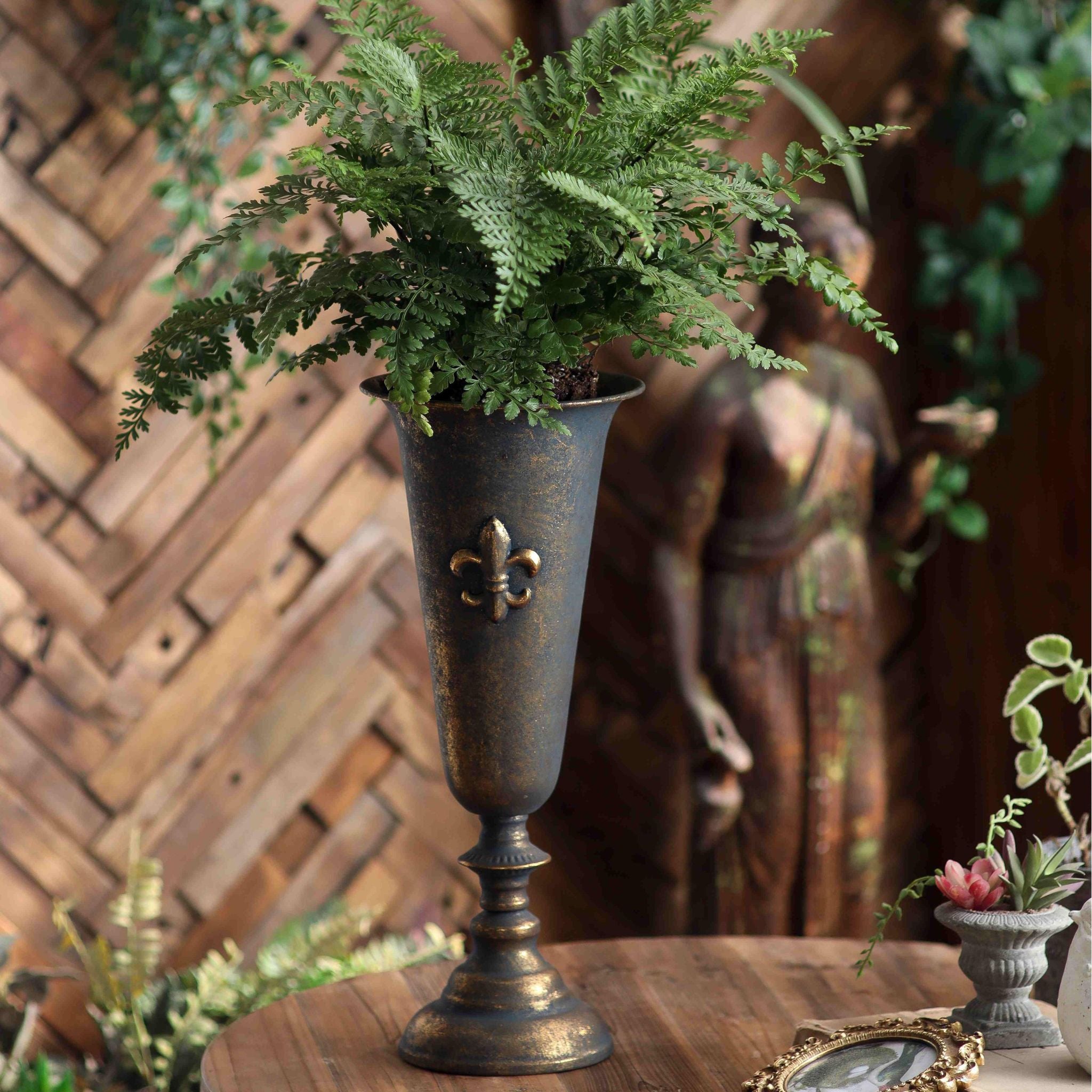 Guido fleur de lis urn vase in aged bronze finish holding a fern on a round table