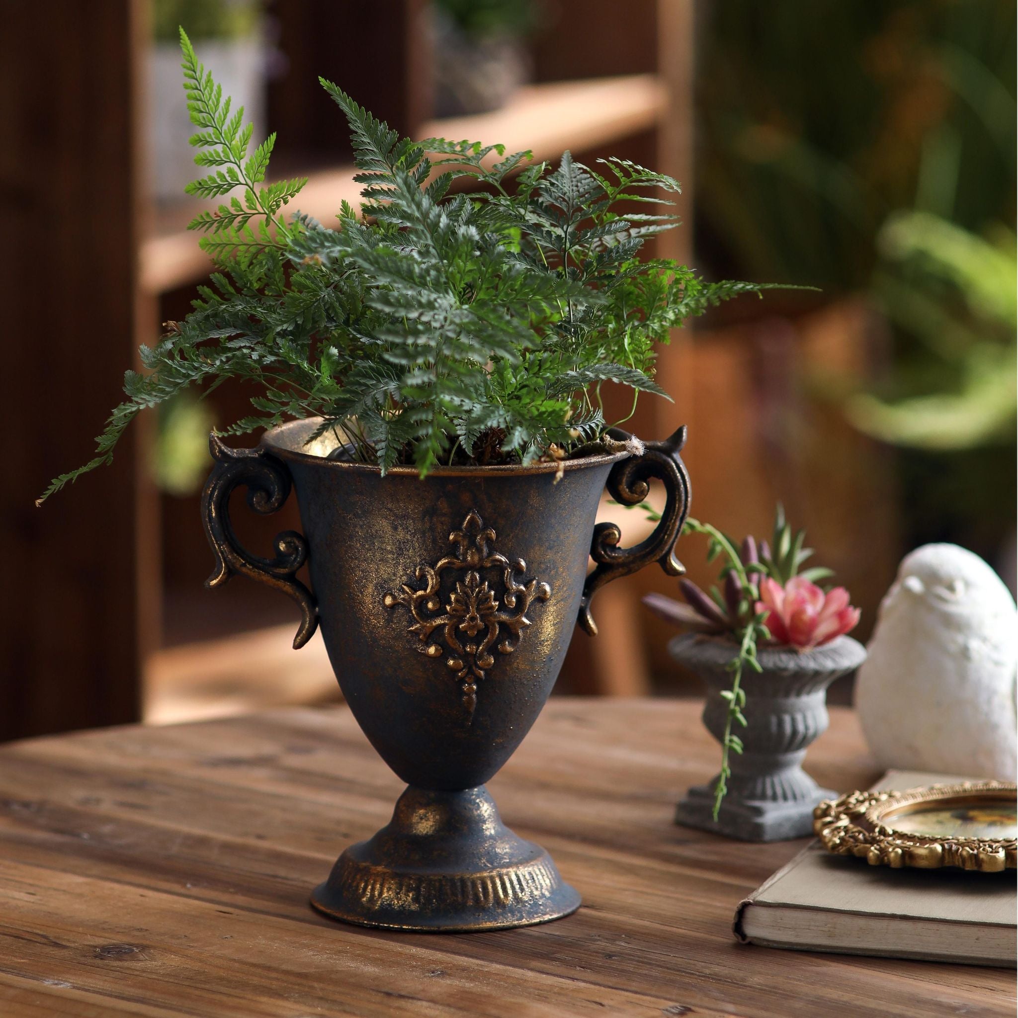 Isla goblet urn in bronze style finish with damask relief holding a fern on a table