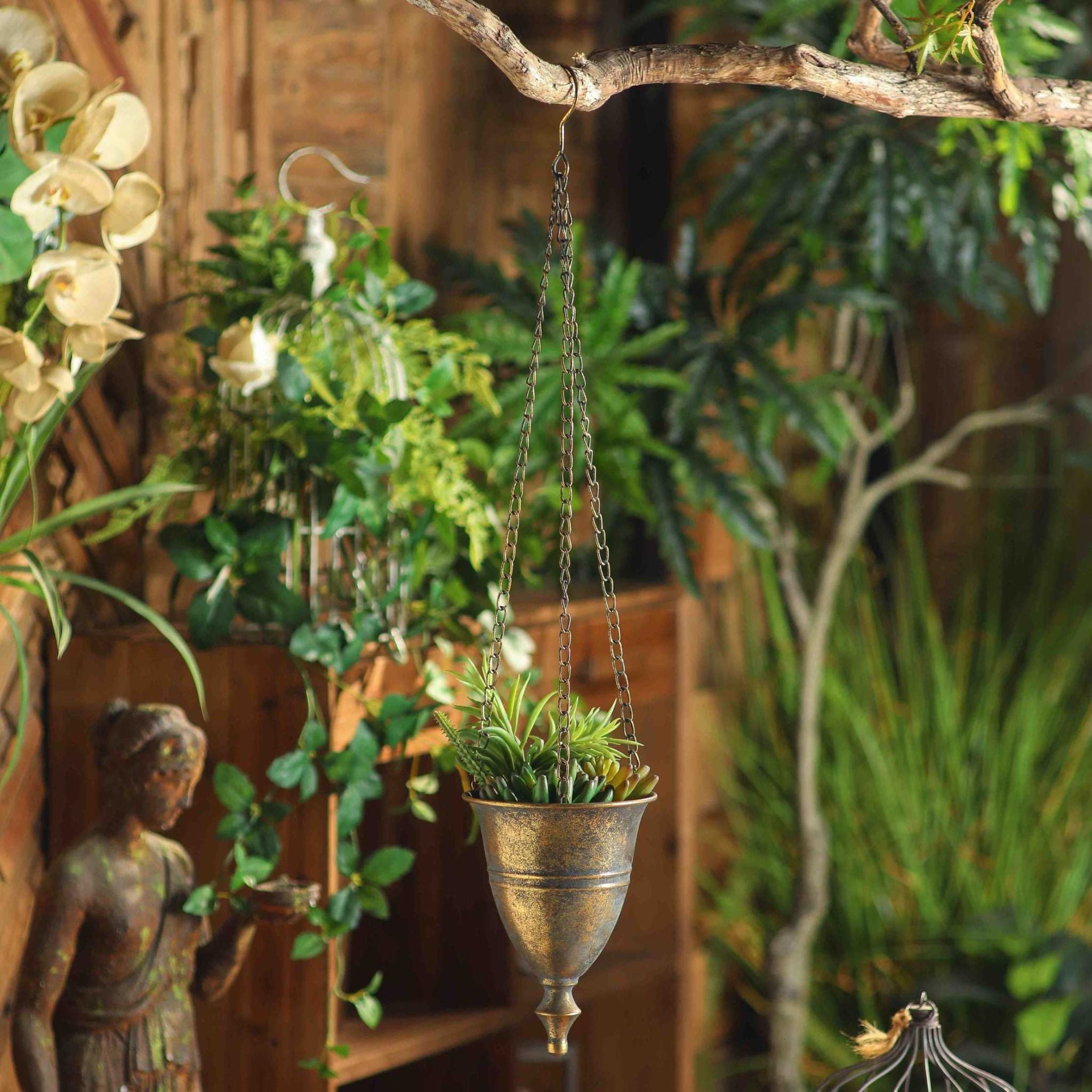 Nino hanging urn planter in antique gold with succulents hanging from a branch