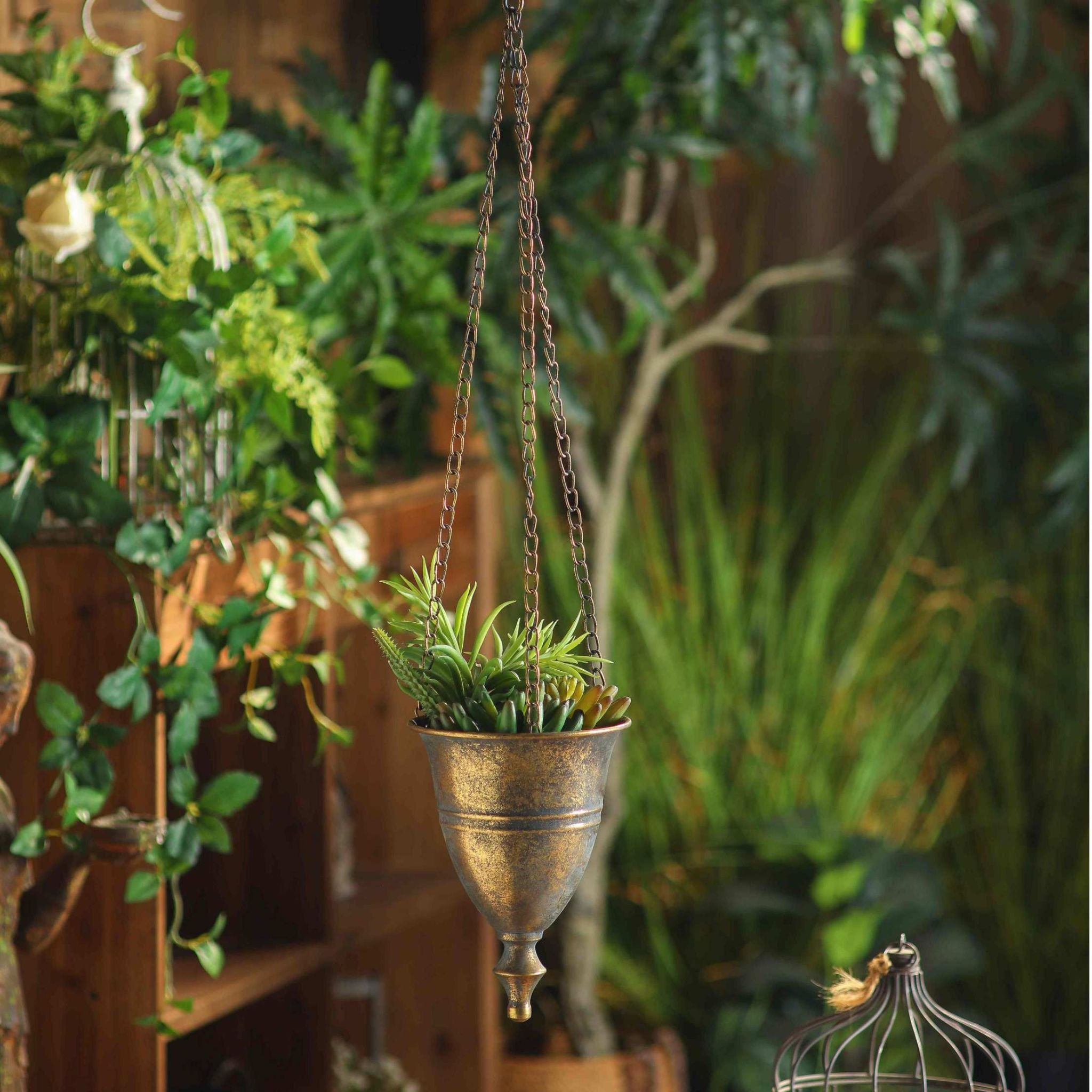 Nino antique gold hanging urn in a garden room full of greenery