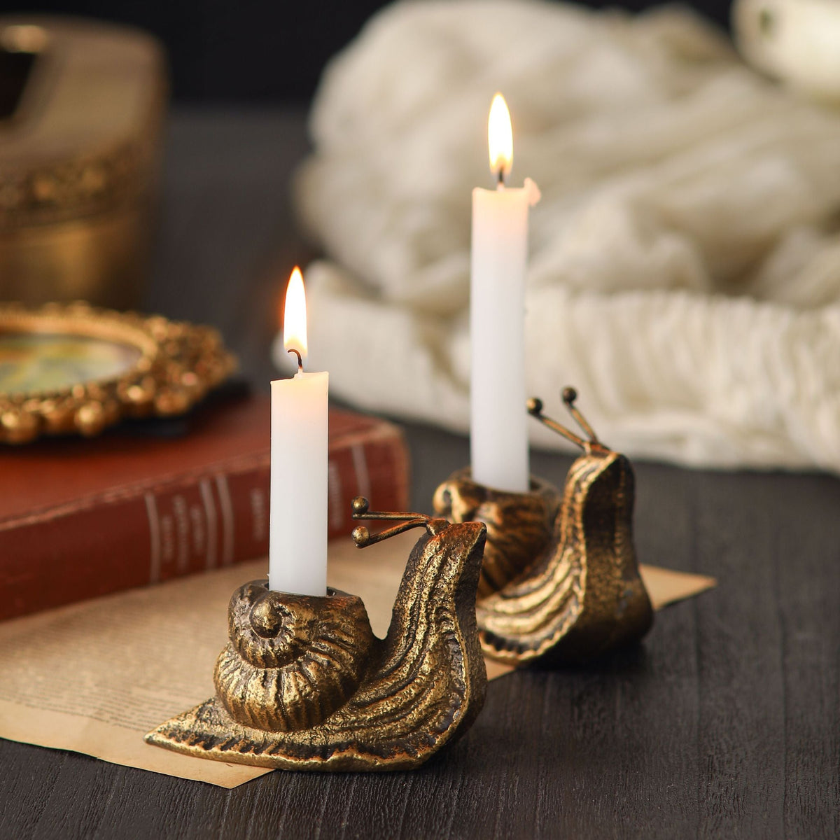 Monsieur and Madame Escargeaux French provincial snail candle holders in aged gold iron, pair lit with white tapers beside antique books