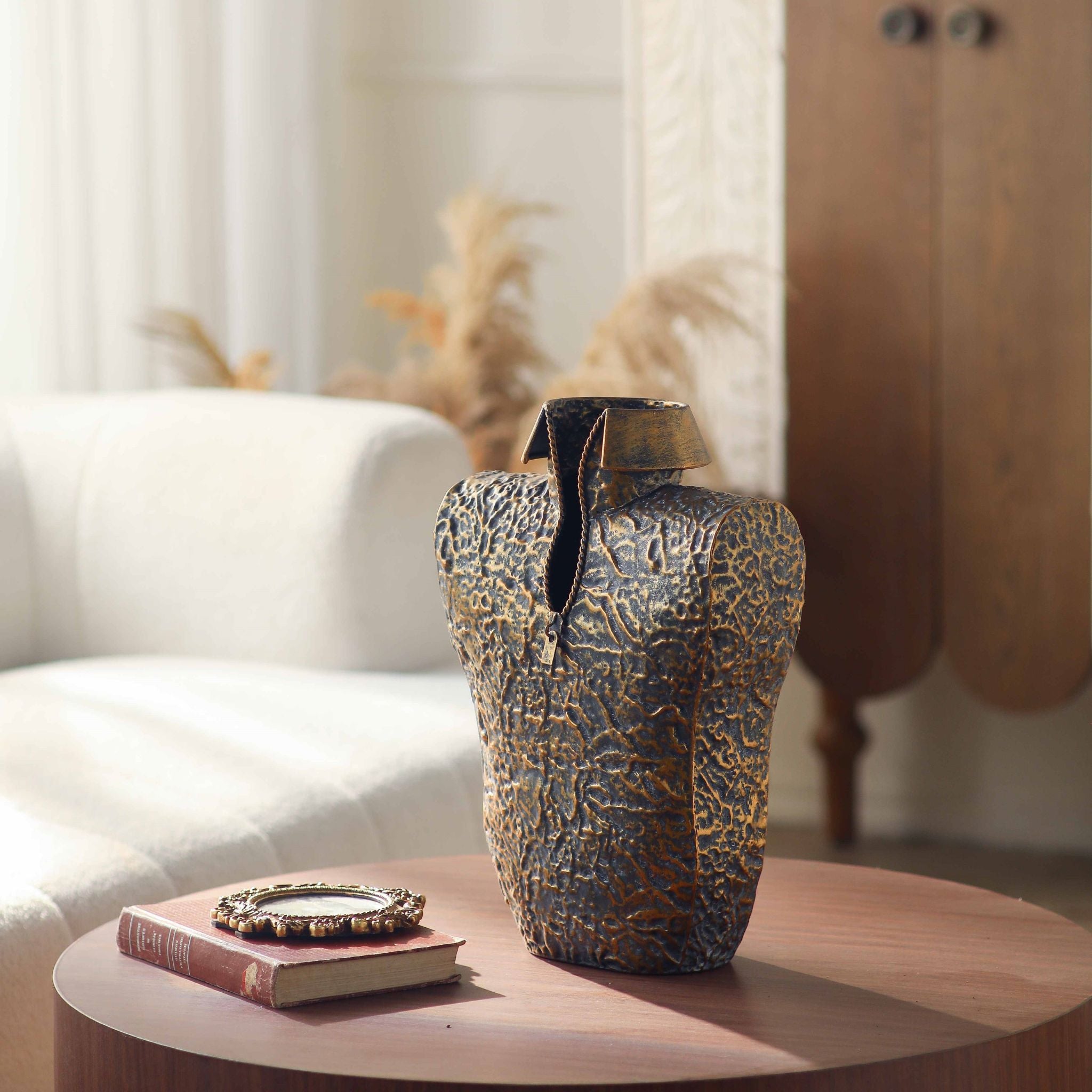 Aldo sculptural torso vase holding bare branches beside a white armchair