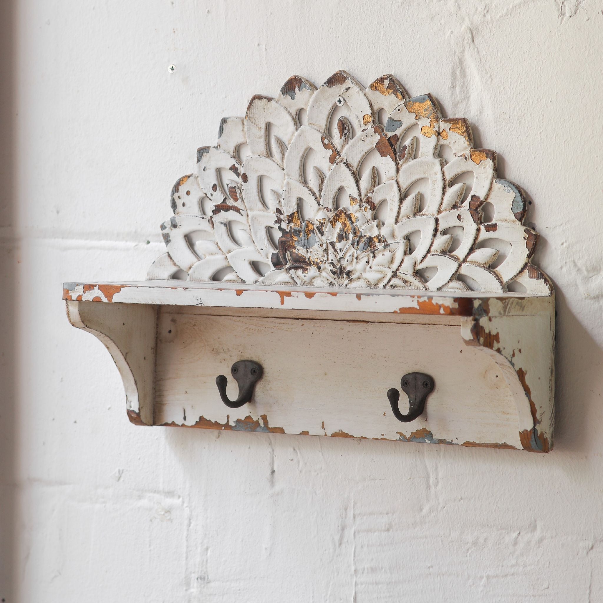 Elio carved crest wall shelf styled on a white wall with a candle and cherub statue nearby