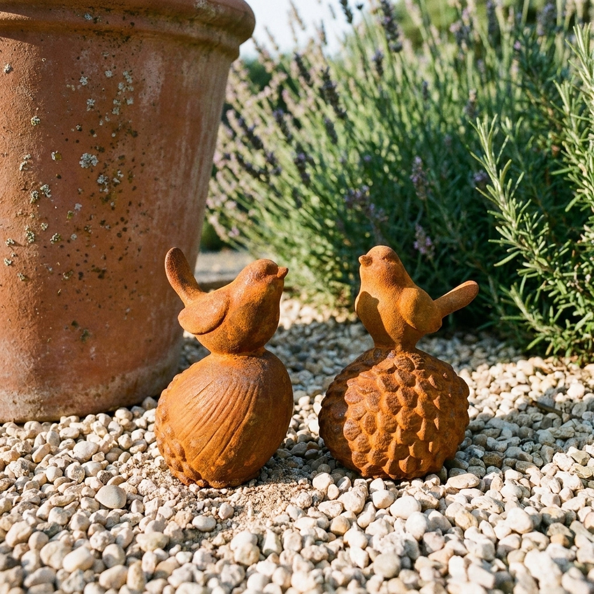 Robin and Sparrow rust cast iron garden birds on an acorn and a pinecone, on gravel beside a terracotta pot