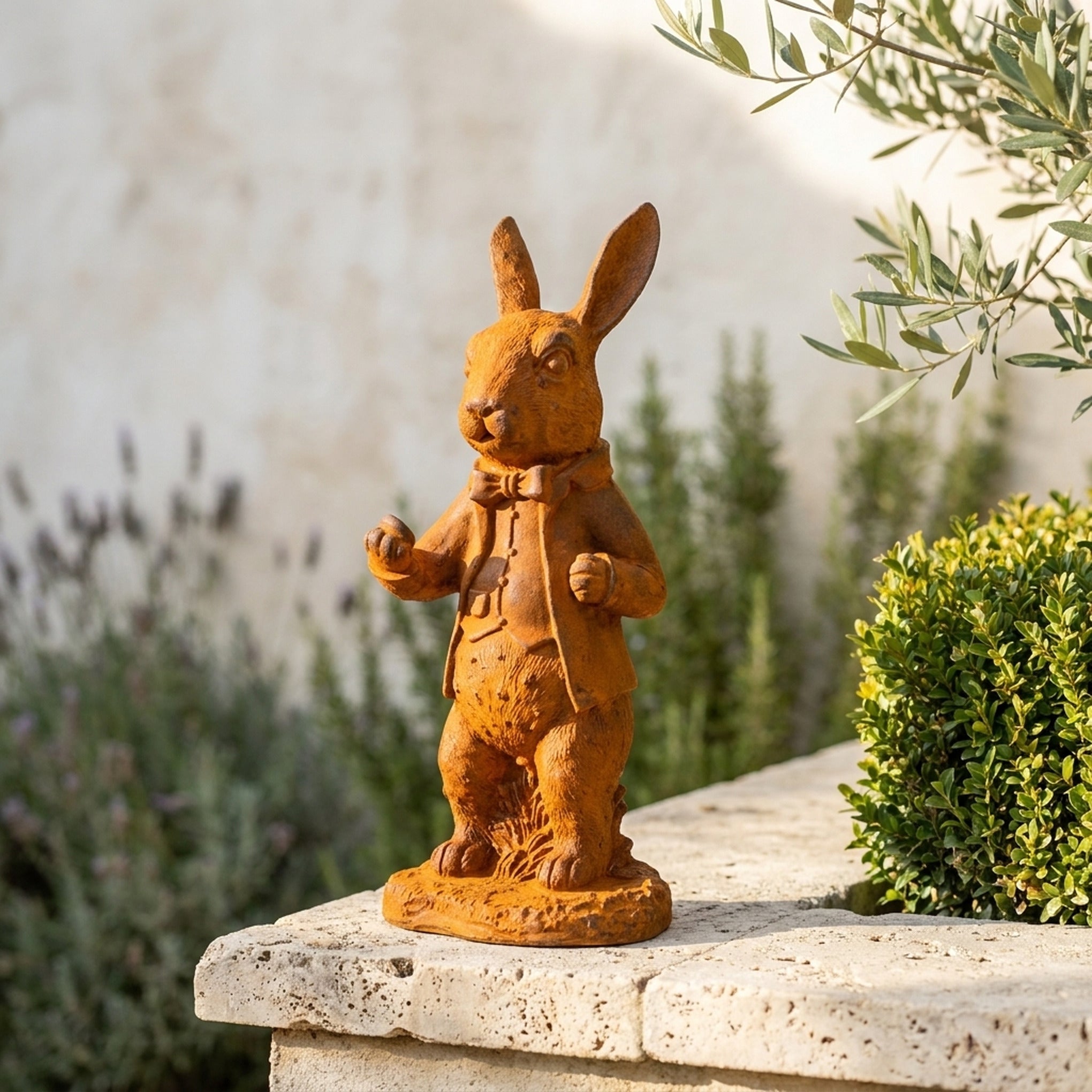 Doctor Bramble rust cast iron rabbit statue in a frock coat on a travertine garden wall with lavender and box hedging