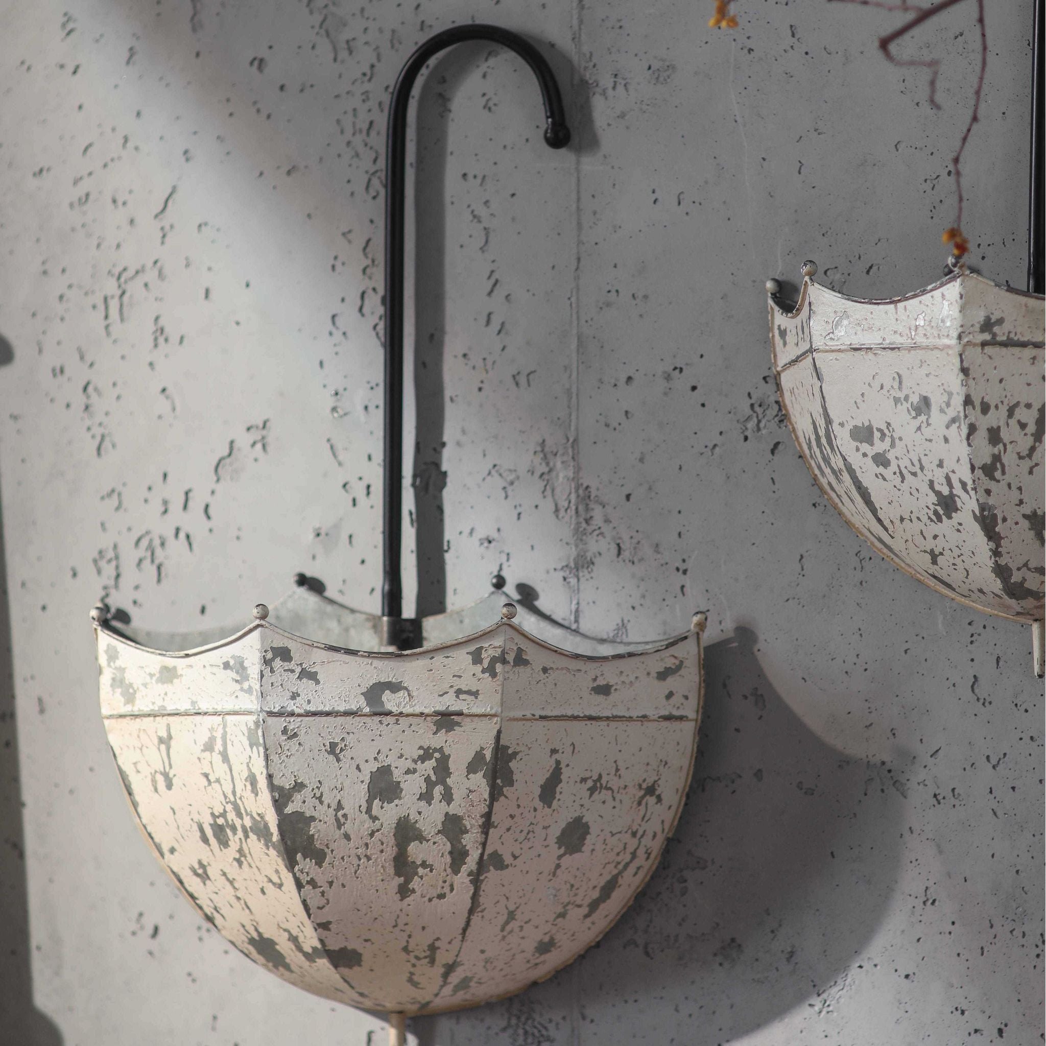 Detail of the larger Parapluie umbrella planter showing chippy distressed cream paintwork over dark iron, with the second smaller umbrella visible to the right