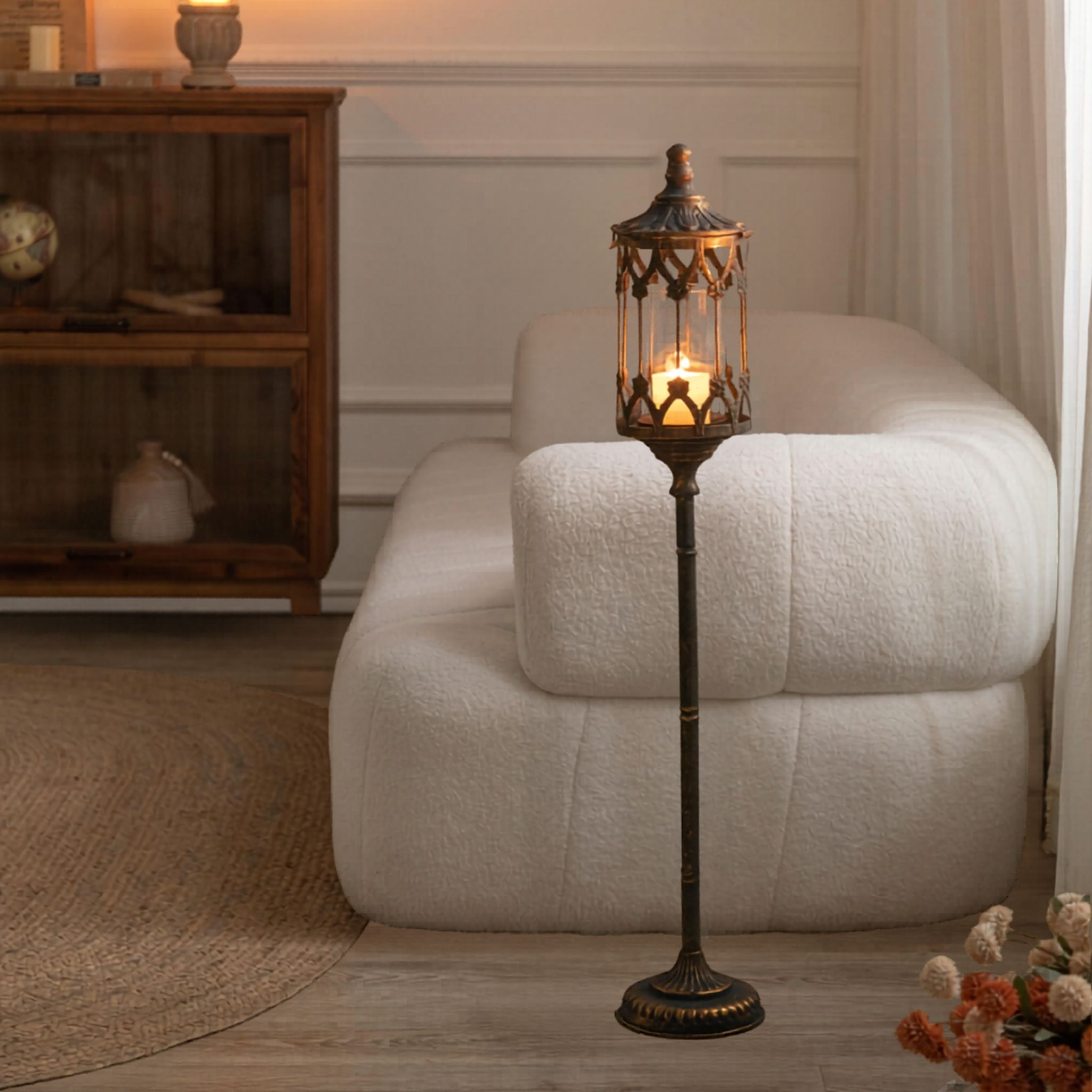 Tall floor candle lantern glowing beside a sofa in a styled room