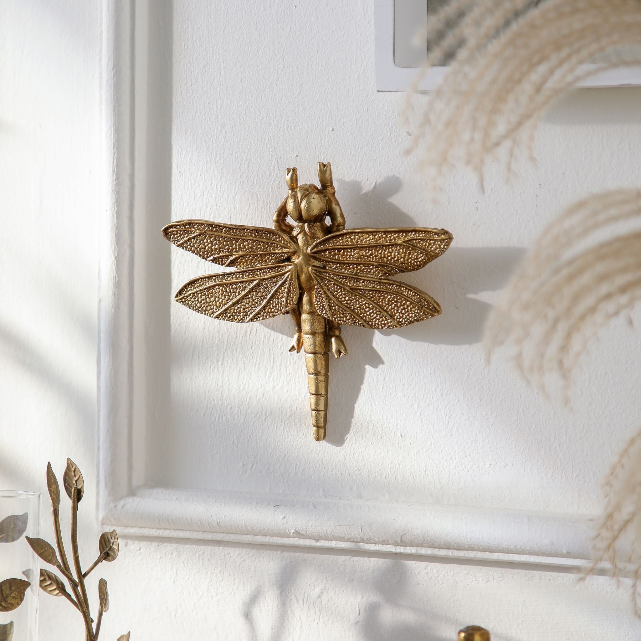 Lidia dragonfly wall decor in antique gold resin mounted on a white panelled wall. Hero.