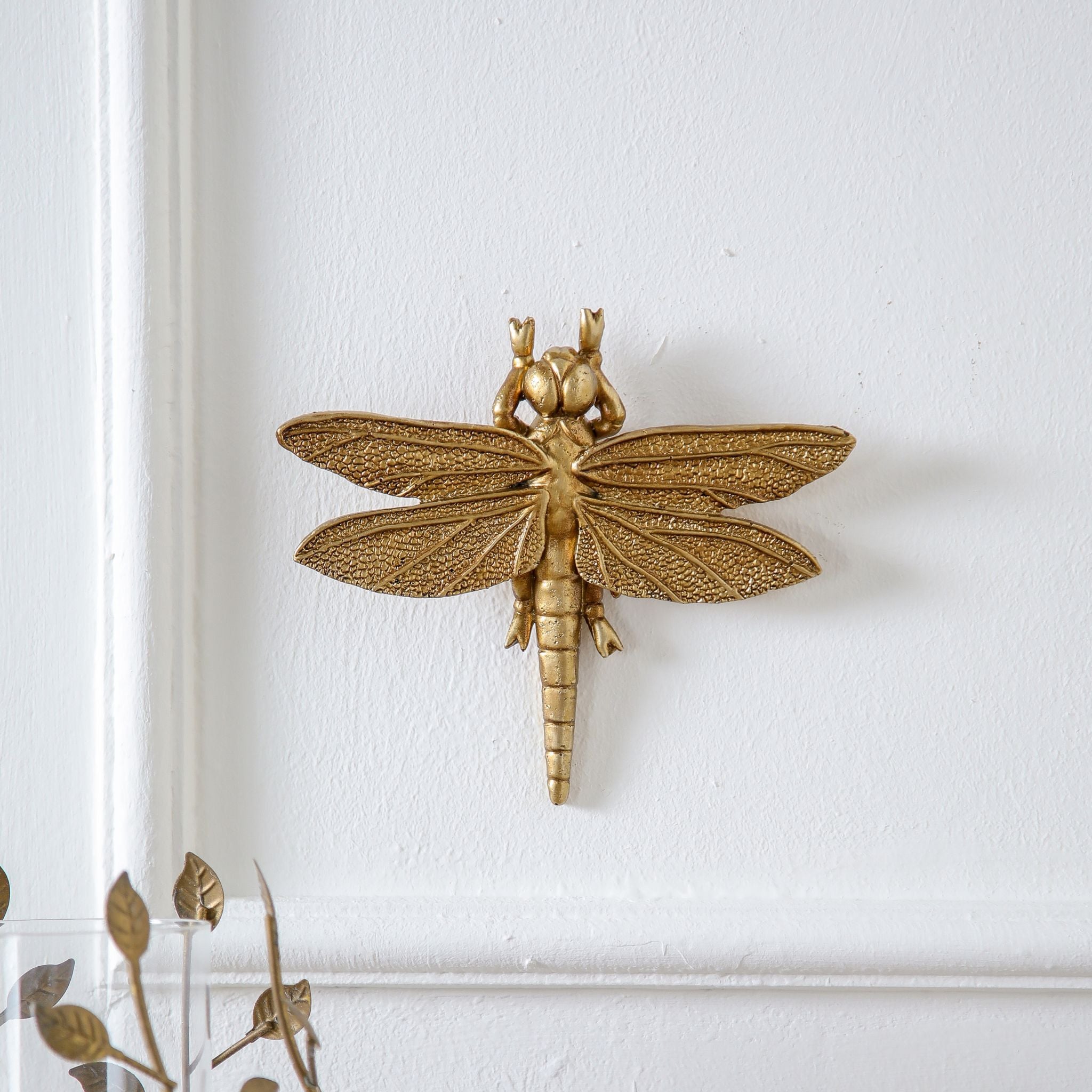 Lidia antique gold dragonfly casting a soft shadow on a white wall panel