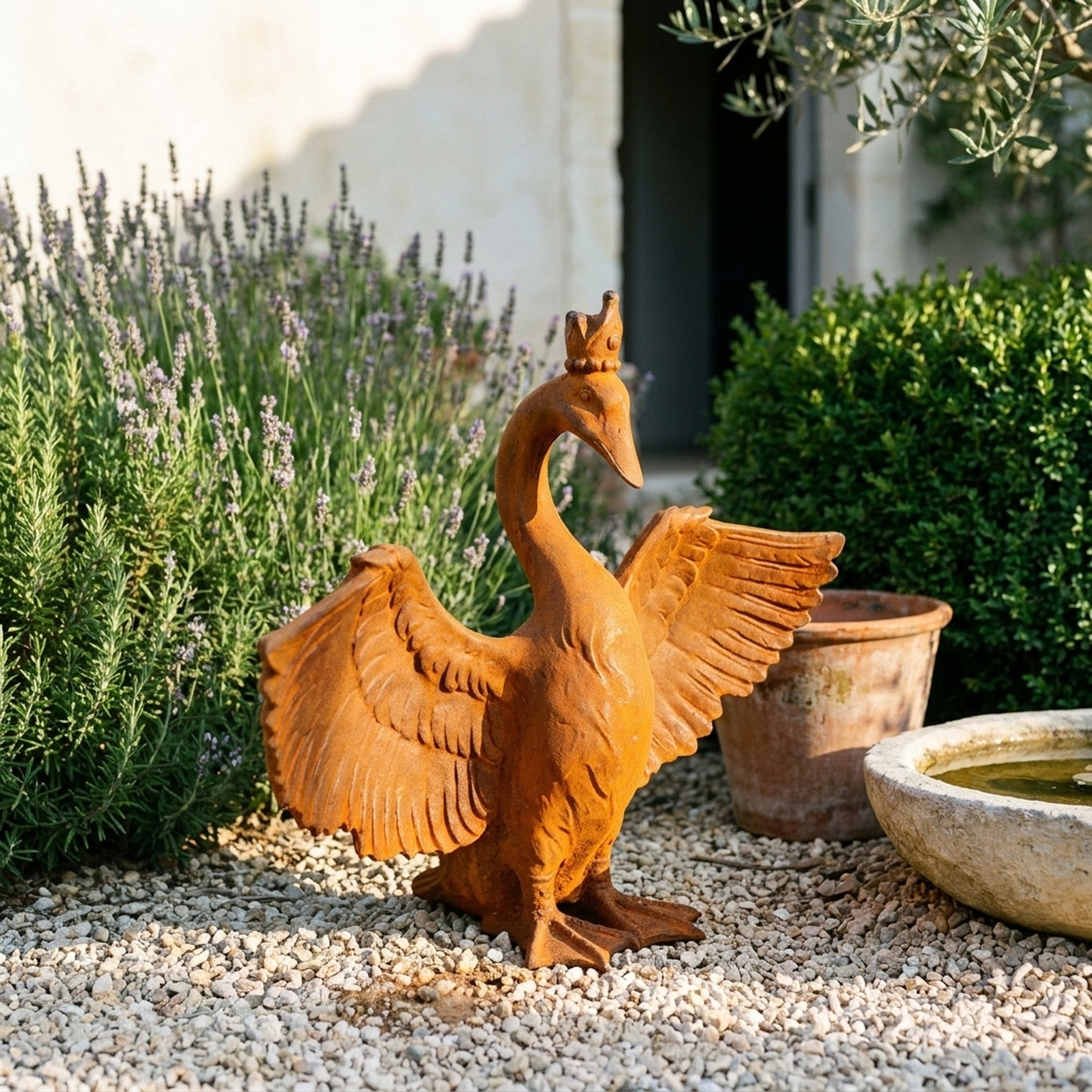 Princess Evangeline rust cast iron crowned goose with wings spread on gravel beside lavender and a stone water basin