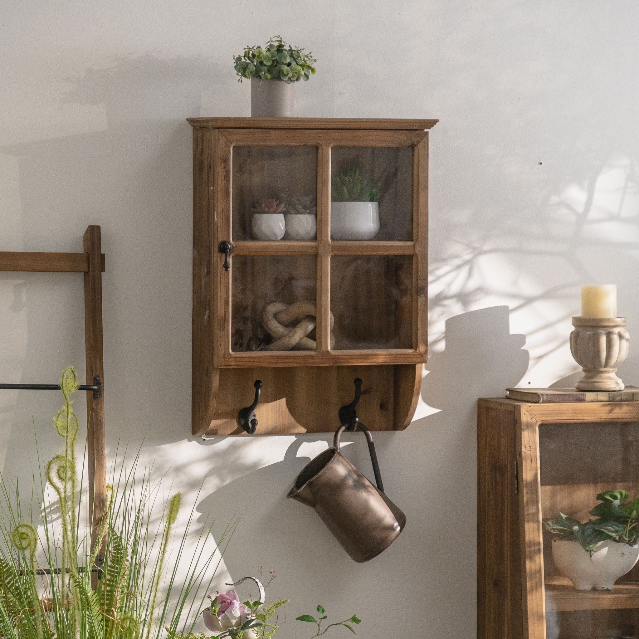 Alain glazed wall cabinet styled in a rustic room, plant on top and a jug hanging from a hook.
