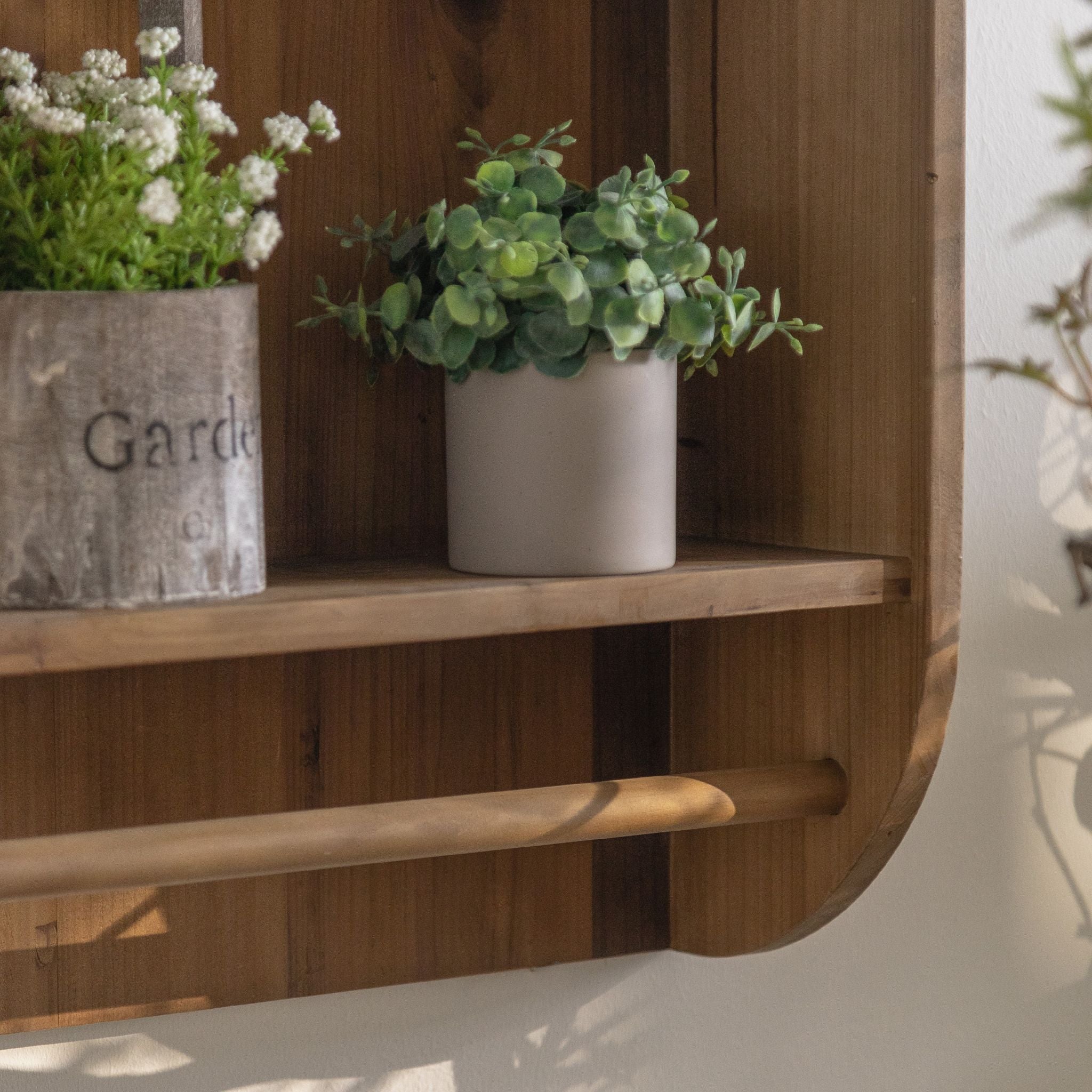 Alderic wall shelf, close detail of the lower shelf with potted plants and the rail running beneath it.