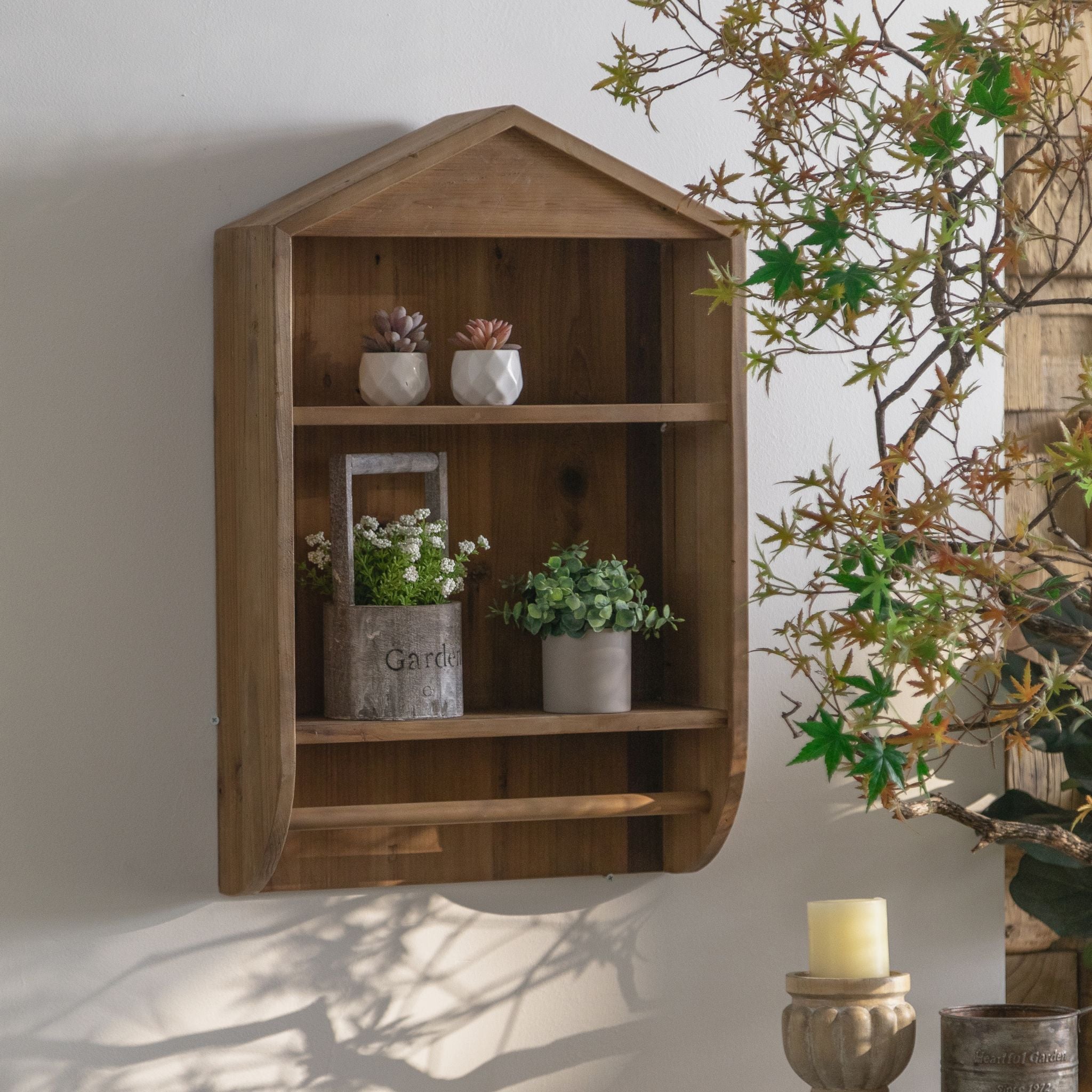 Alderic timber wall shelf at an angle, showing the rounded sides and the single rail beneath the lower shelf, styled with plants.