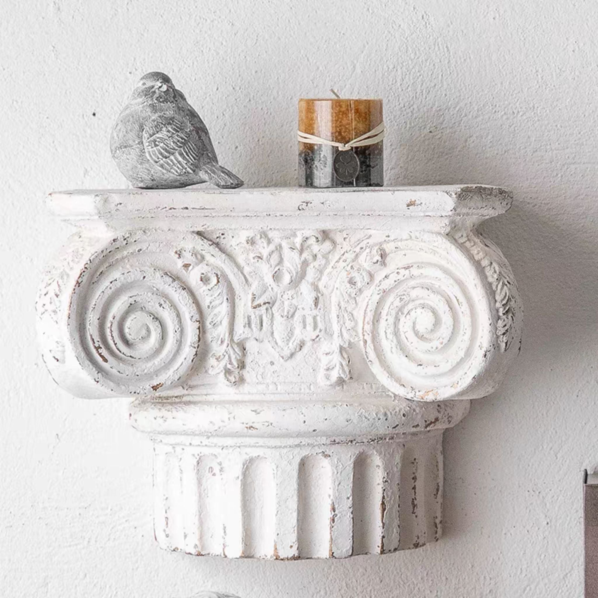 Aline corbel wall shelf mounted on a wall holding a pillar candle and a small bird ornament.