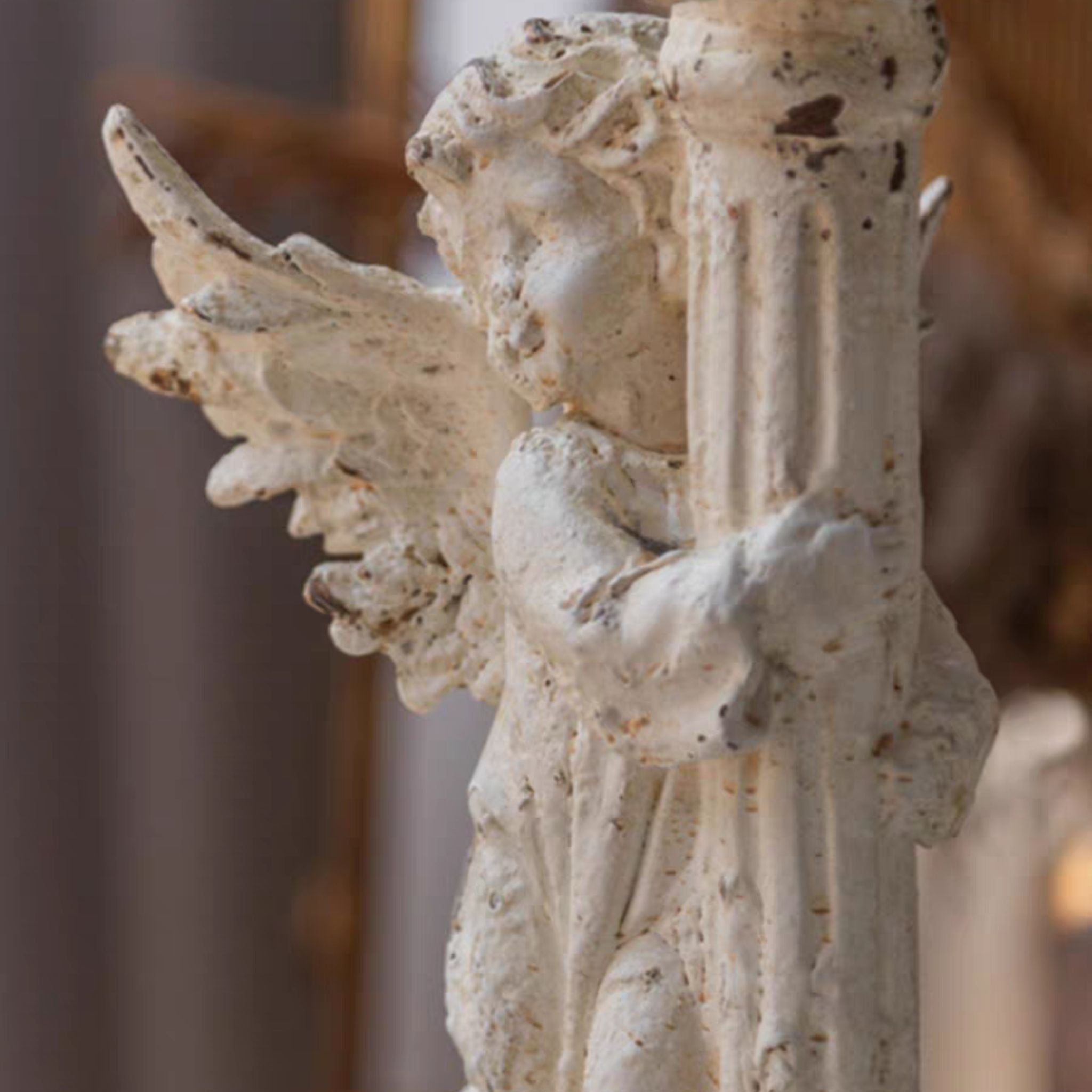 Close-up of the André cherub's face and wing against the fluted column, showing the chipped antique-white finish worn through to terracotta.