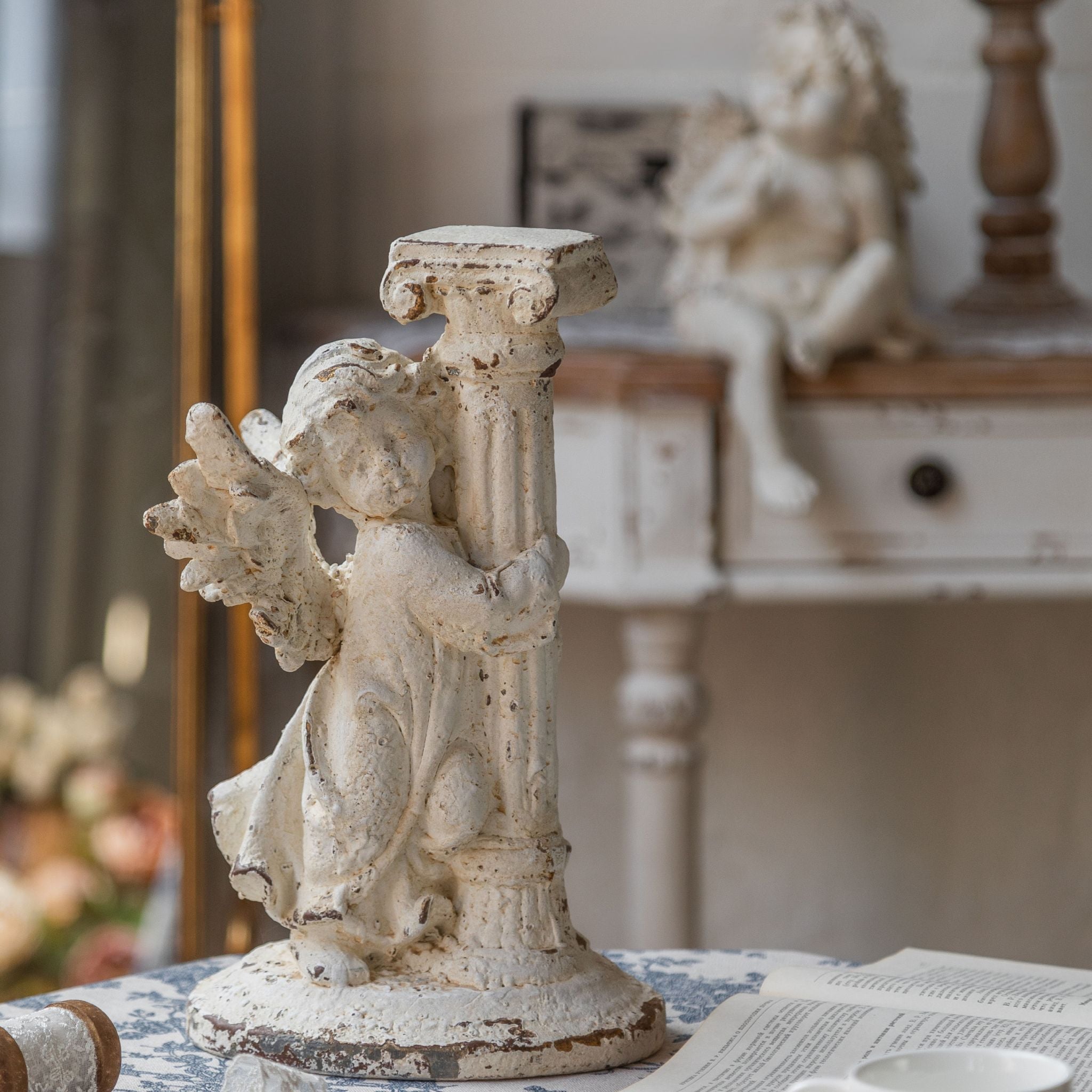 André French Provincial cherub sculpture in distressed antique white, winged figure clutching a fluted column, styled on a console with a mirror behind. Hero.