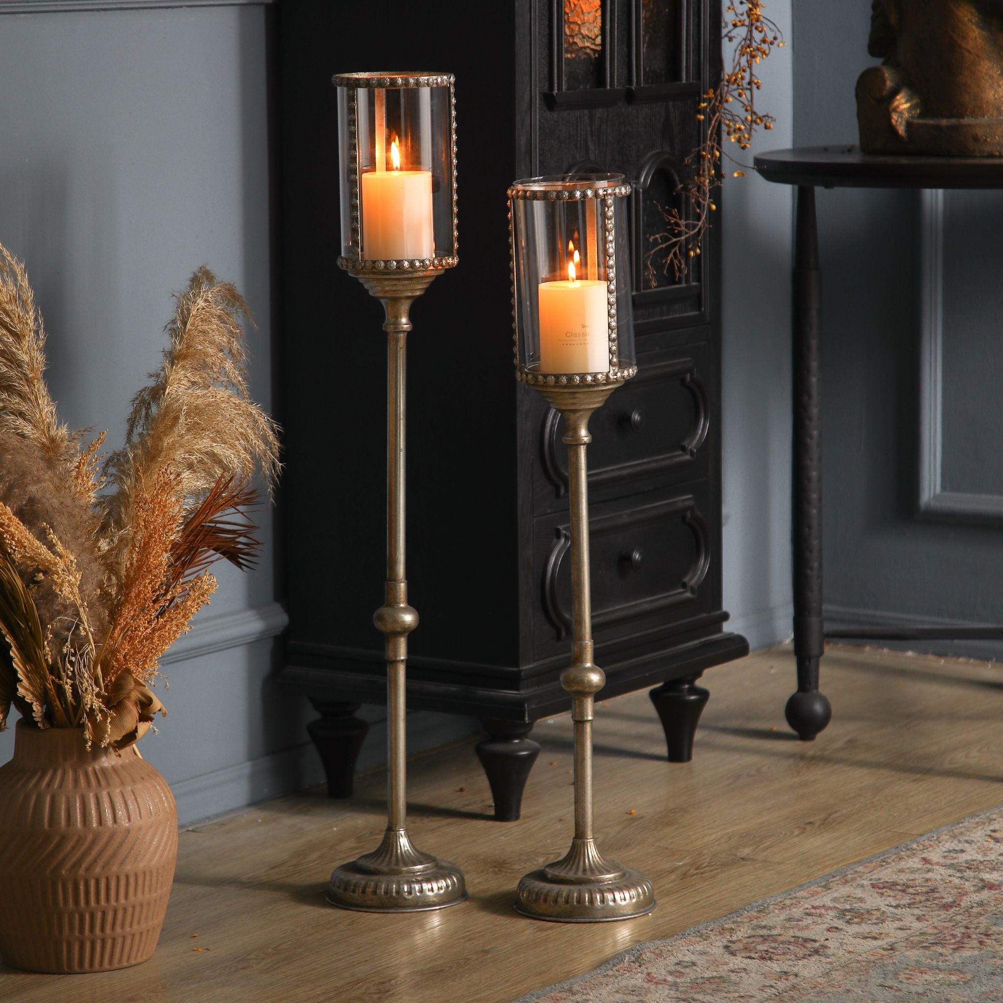 Pair of antique gold floor candle holders lit at floor level beside a black cabinet.