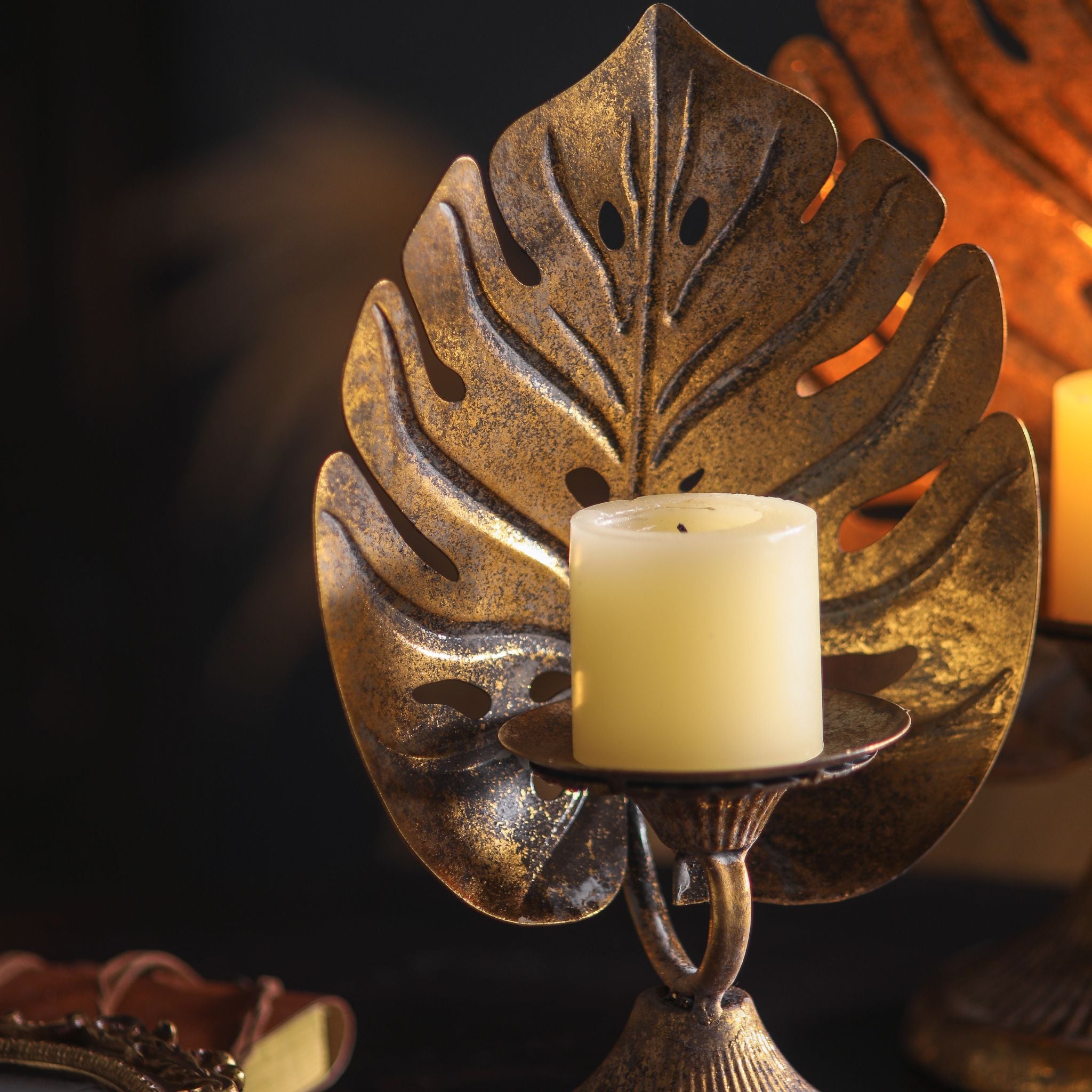Monstera leaf candle holder lit with a cream pillar candle, pierced leaf backplate in antique gold.