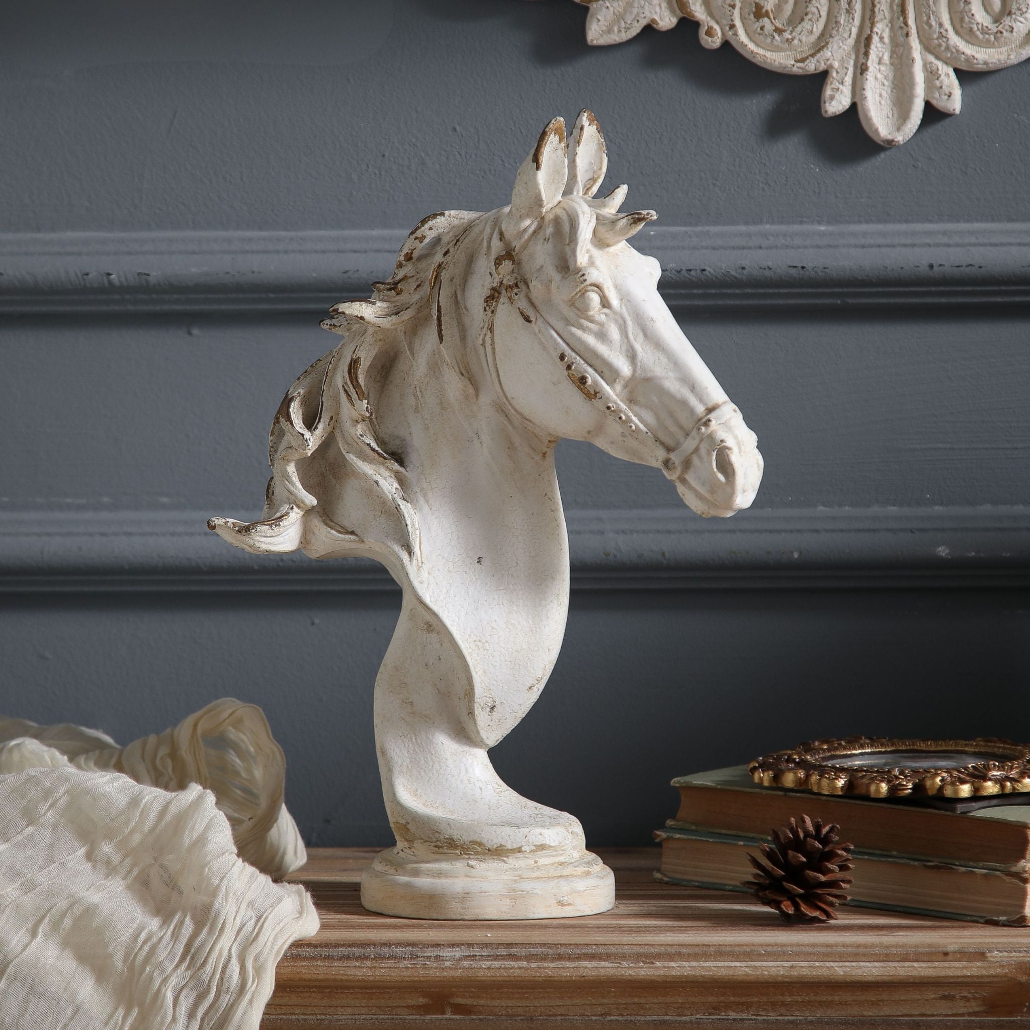 Apollon horse head bust styled on a wood console with antique books, vintage gilt frame, pine cone, and dried floral elements