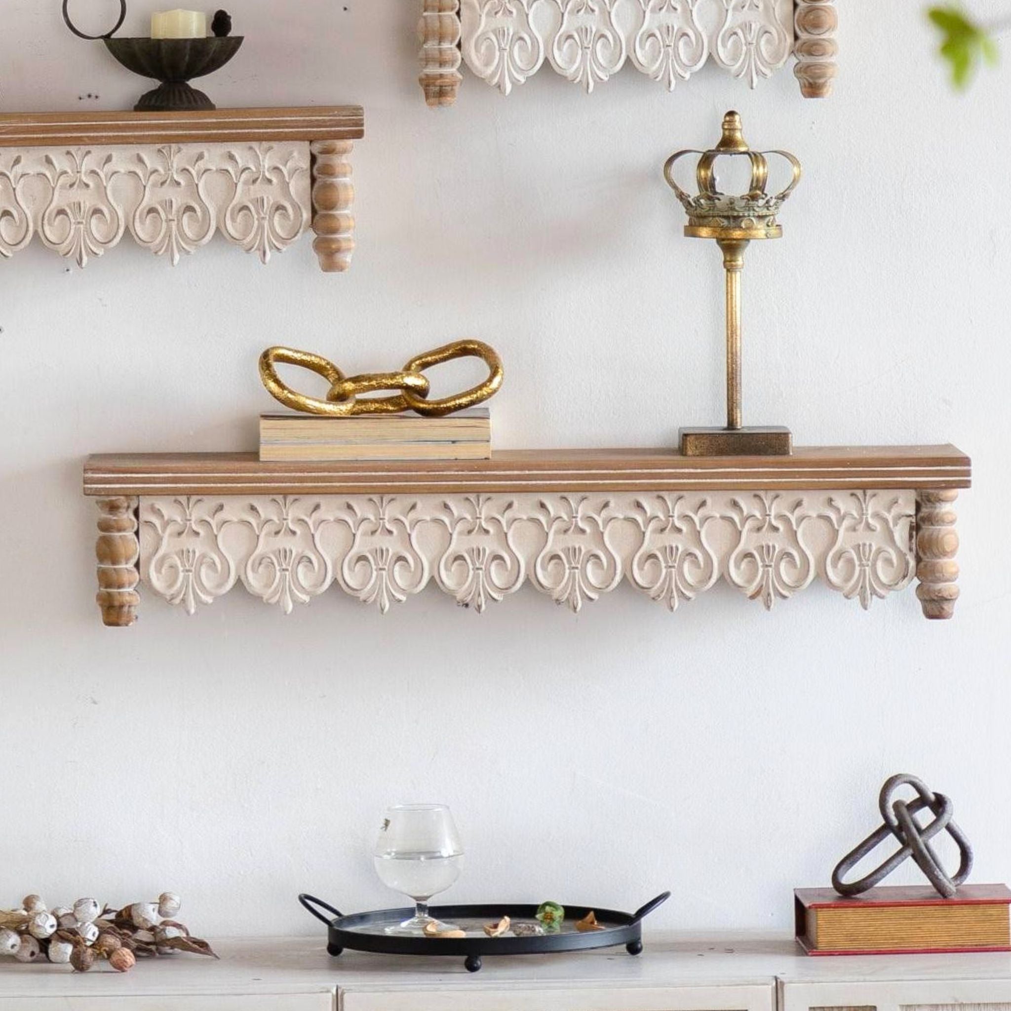 Ariane wide carved-apron wall shelf styled with books and a gold chain link