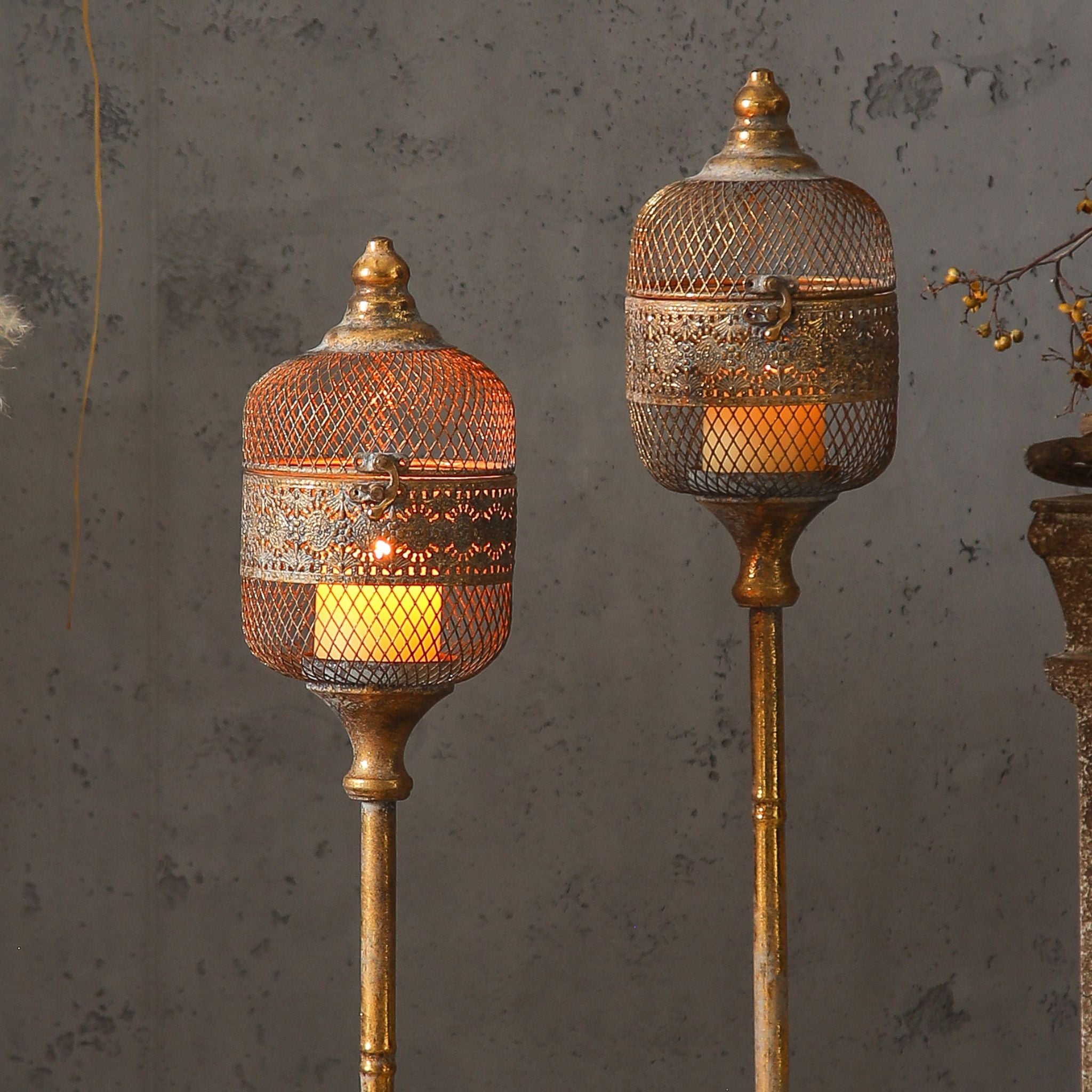 The Astrid and taller Celine lantern heads side by side, both glowing through the antique gold mesh.