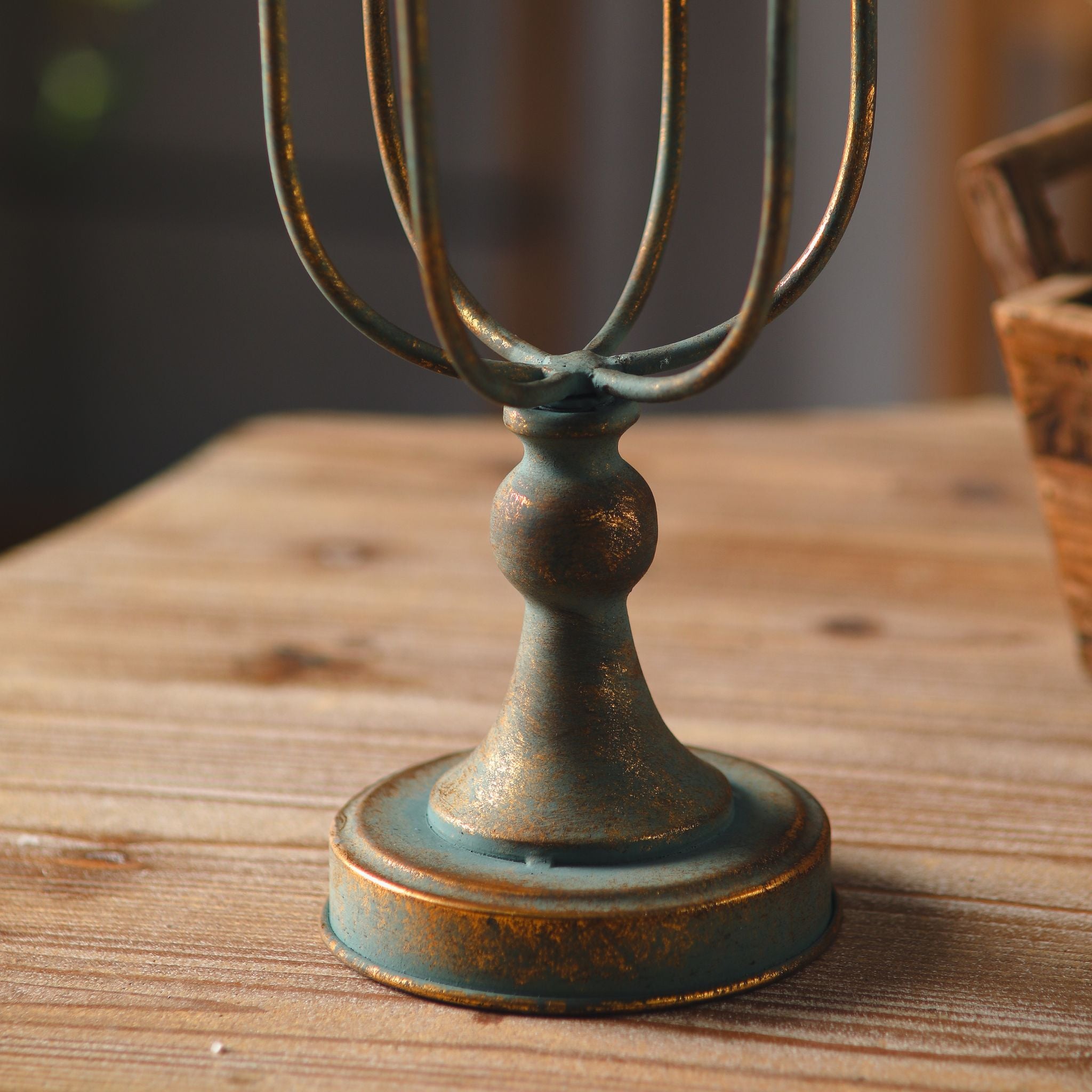 Close-up of the Audrée candelabra turned baluster stem and domed base, antique gold worn over a verdigris base, on a timber surface.