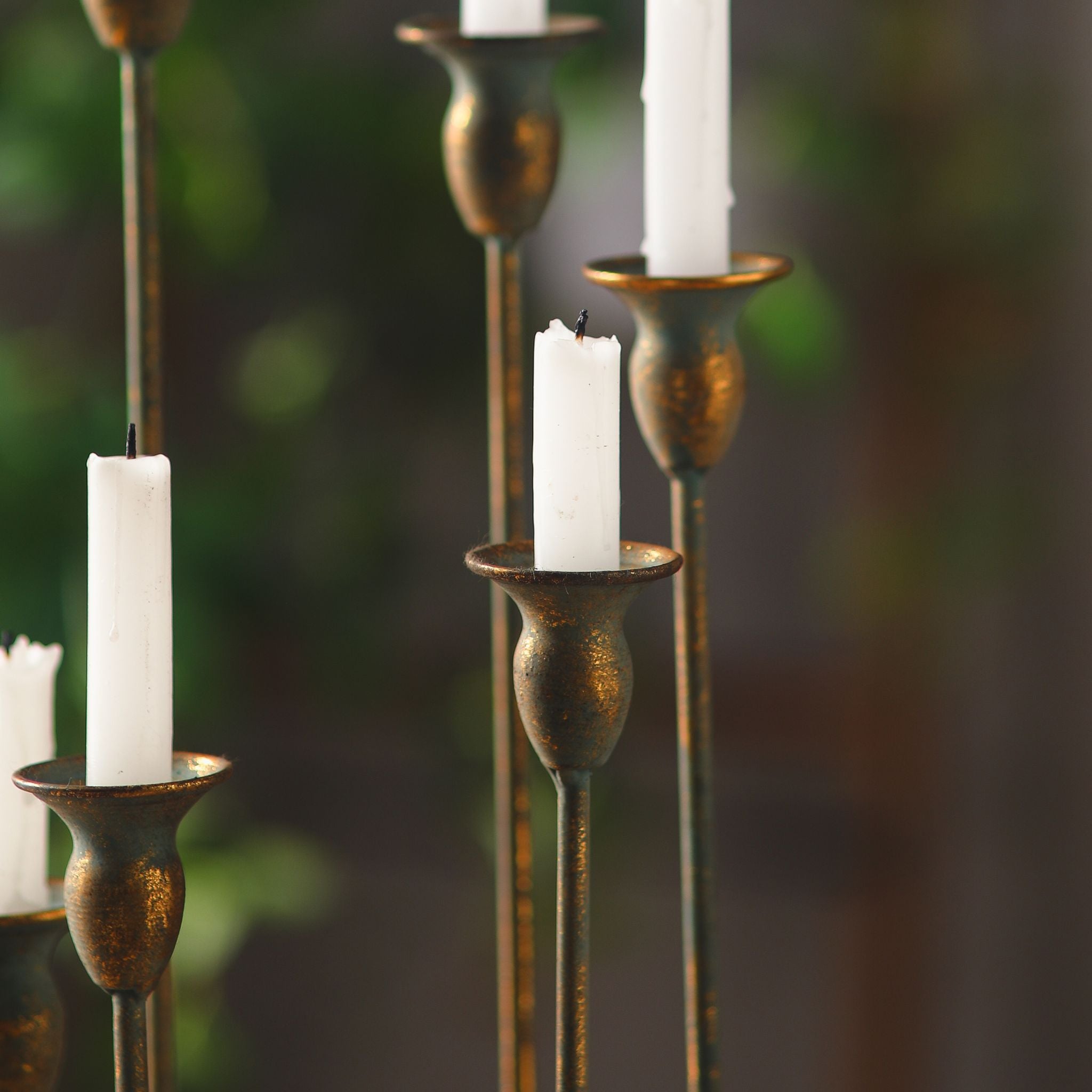 Close-up of the Audrée candelabra trumpet cups holding white taper candles, antique gold finish worn over a teal verdigris base.