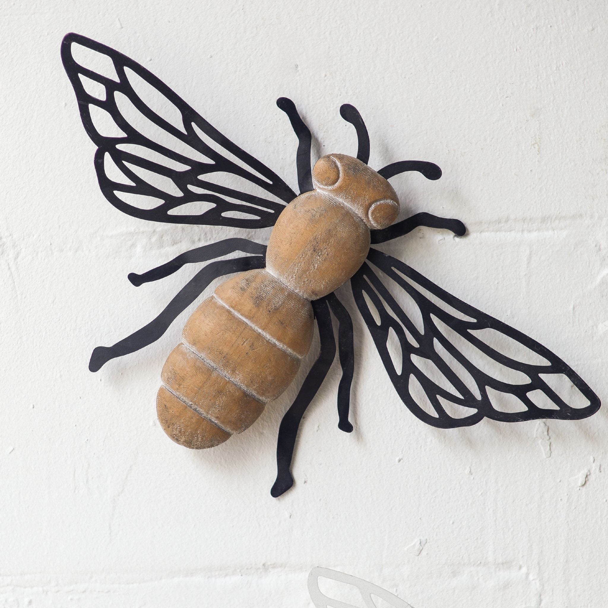 Barry French Provincial bee wall decor with distressed wood body and laser-cut matte black iron wings, mounted solo on a textured white wall. Hero.