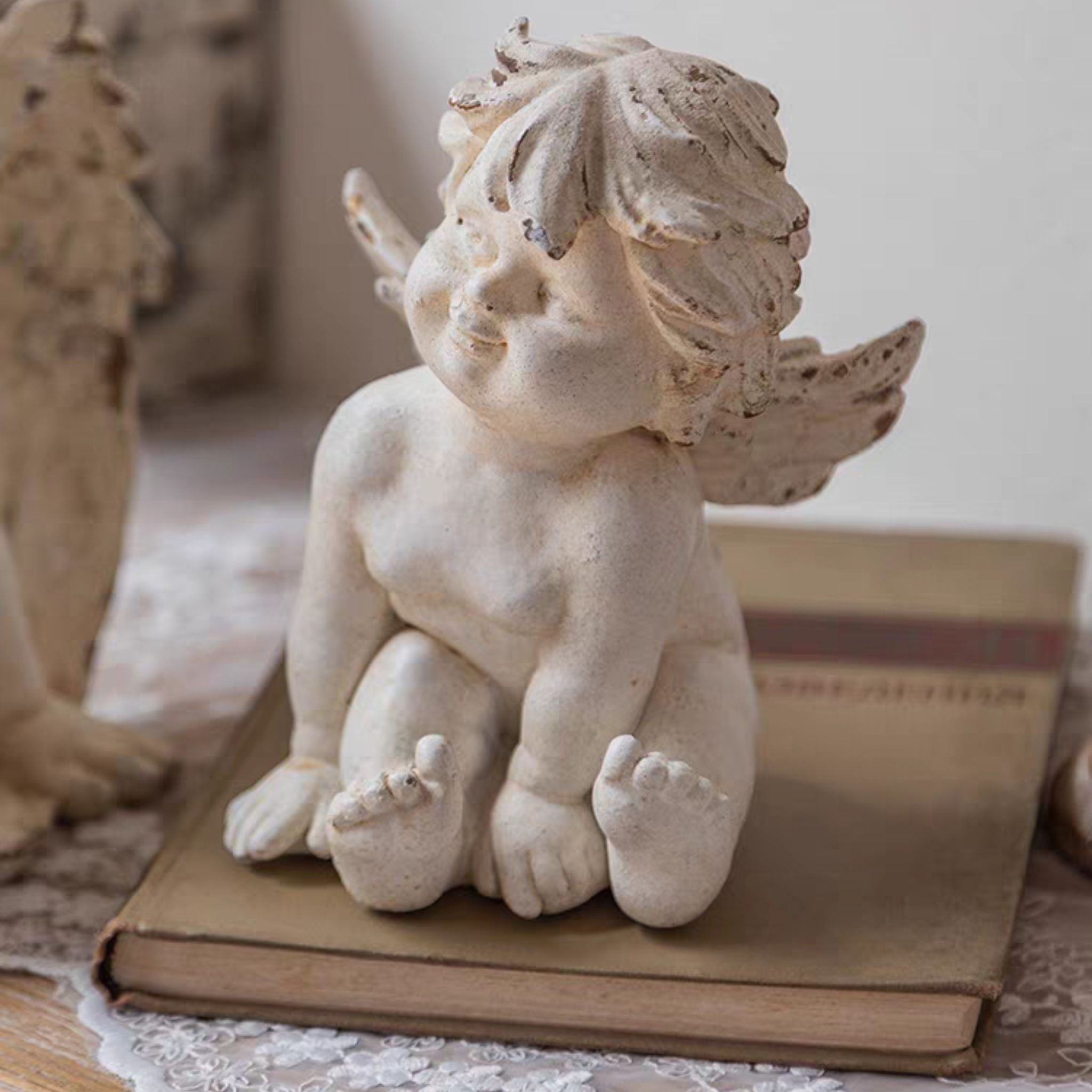 Close-up of Bastien cherub figurine showing the tilted head, soft smile, and distressed whitewash finish on hair and wings