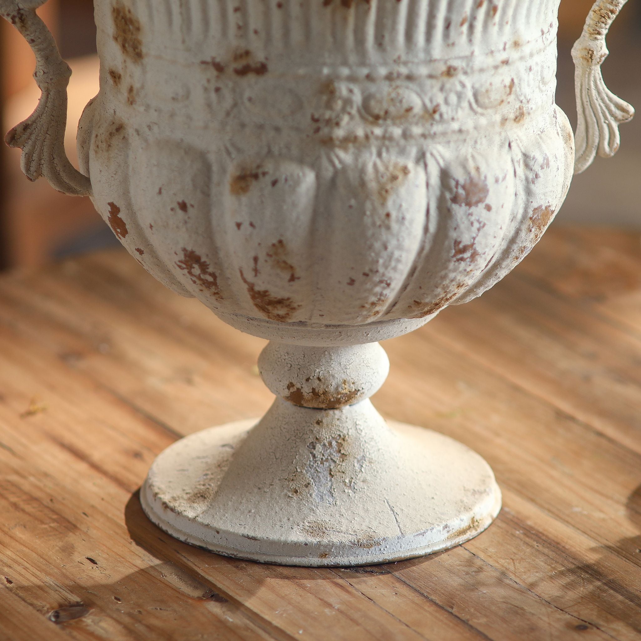 Close-up of the Benoît urn gadrooned lower bowl, banding and turned foot in chipped white and rust.
