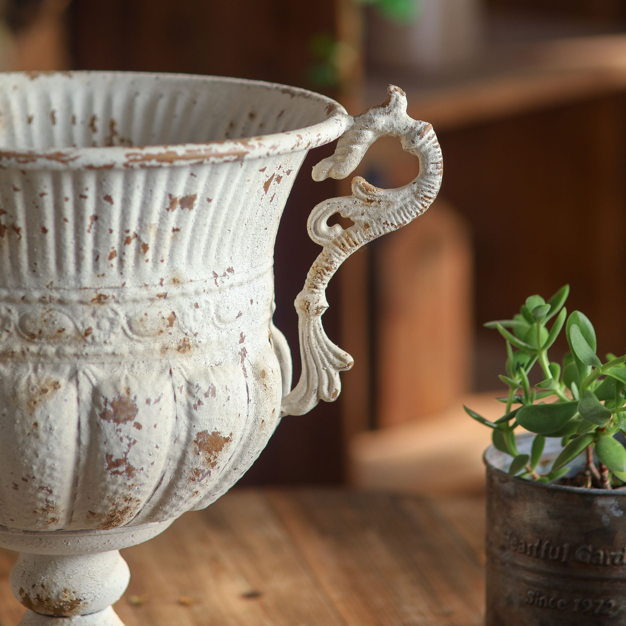 Close-up of the Benoît urn ornate scroll handle and chipped antique-white finish over metal.