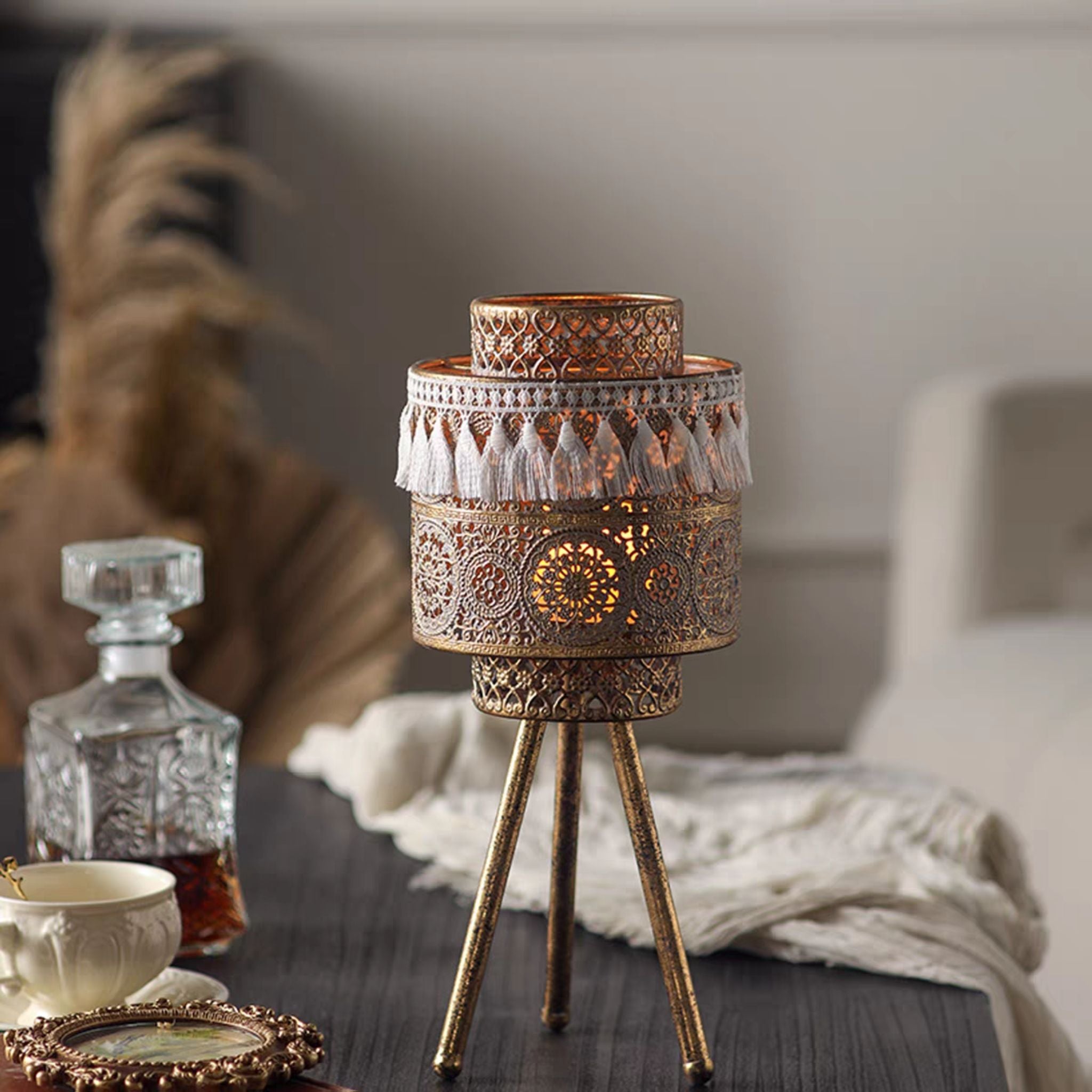Antique gold boho tealight lantern lit on a tripod stand, styled with a decanter and teacup.