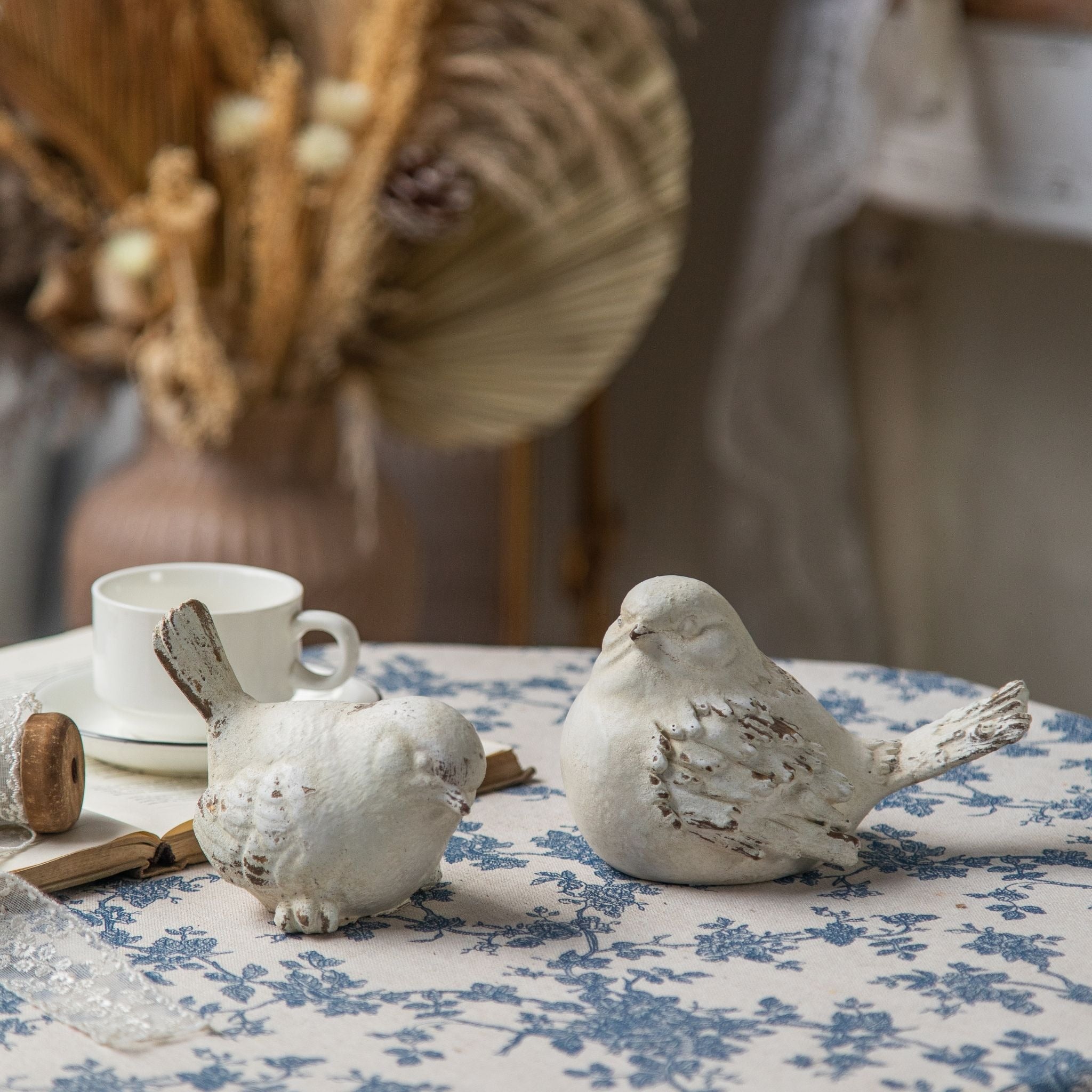 Cameron bird figurines side by side on toile, one settled low and one with a fanned tail, showing the aged stone finish