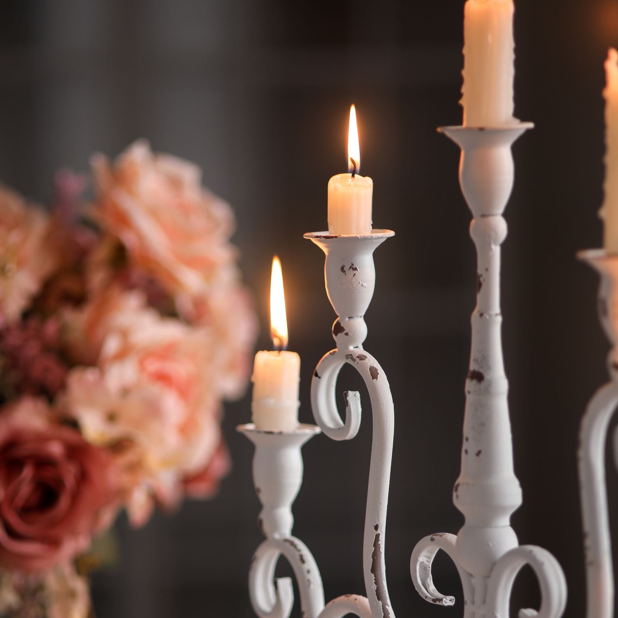 Close view of the candle cups and scrolled arms in distressed white holding lit taper candles.
