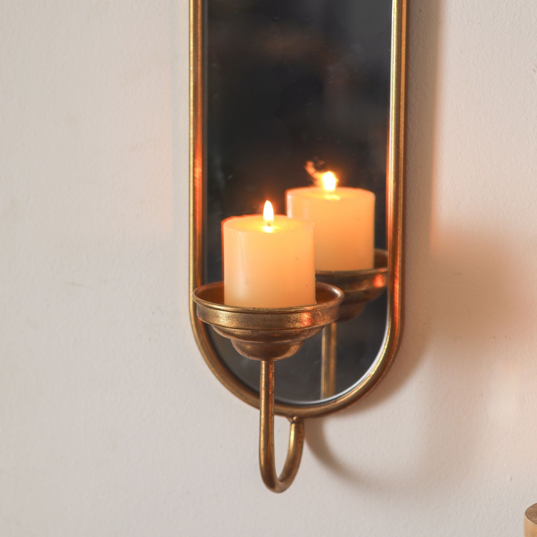 Close-up of the Aude sconce candle cup with a lit candle reflected in the mirror back