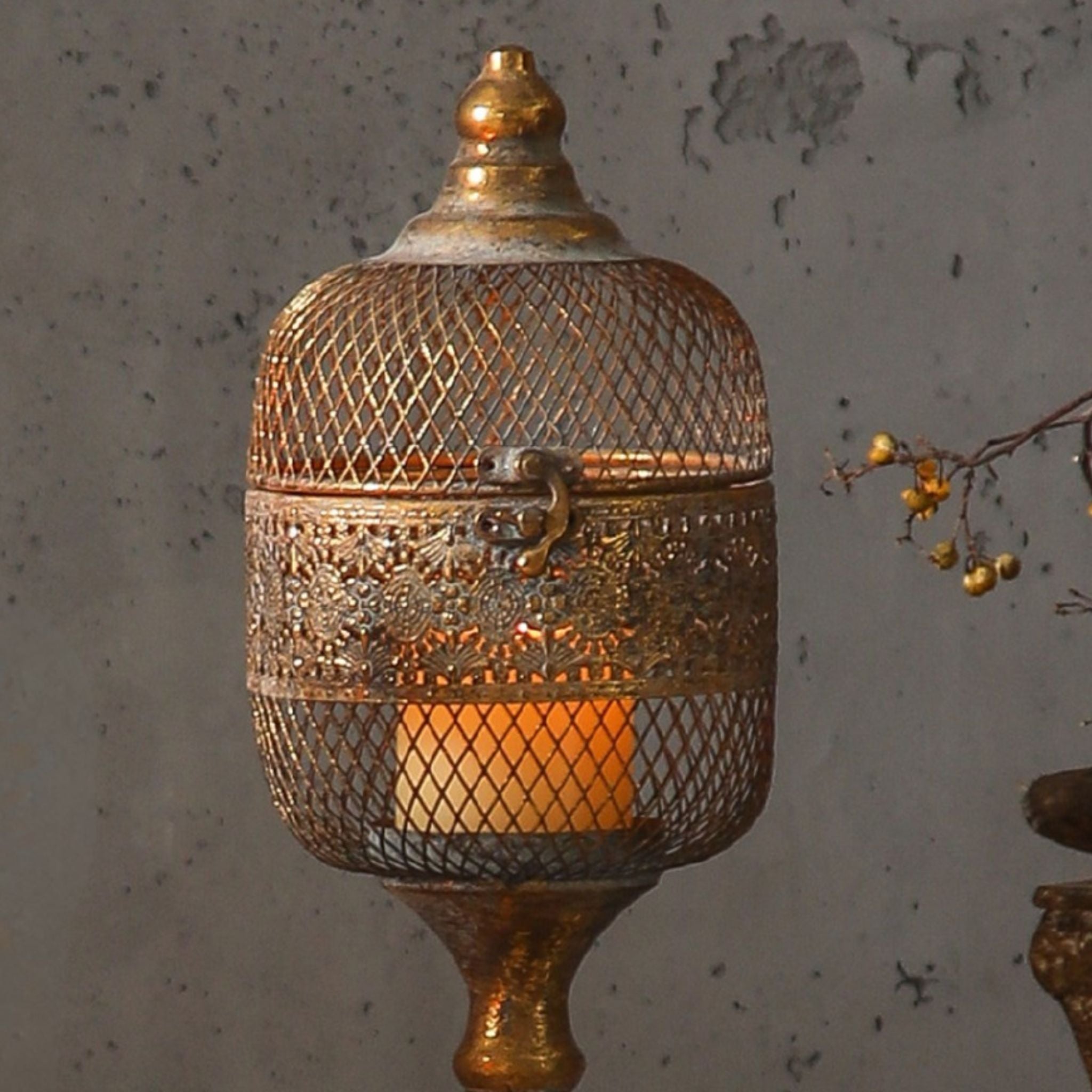 Close detail of the Celine lantern head, elongated diamond mesh dome, embossed openwork band, ring latch and the glass candle cup lit inside.
