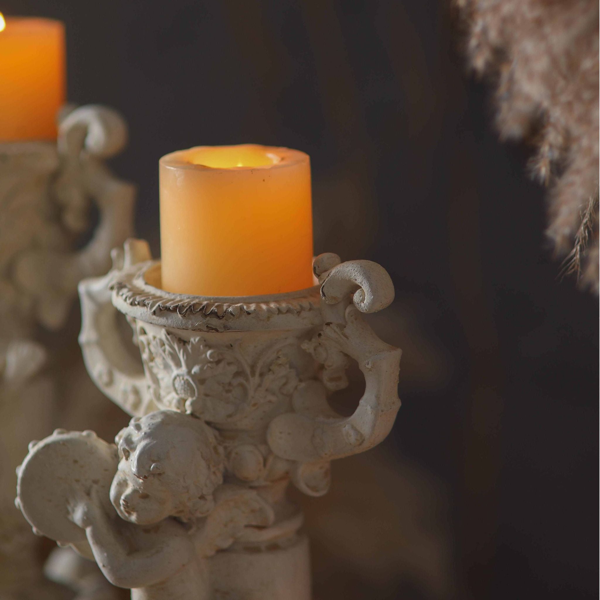 Close-up of the Claude cherub candle holder urn cup and scroll handles holding a lit pillar candle