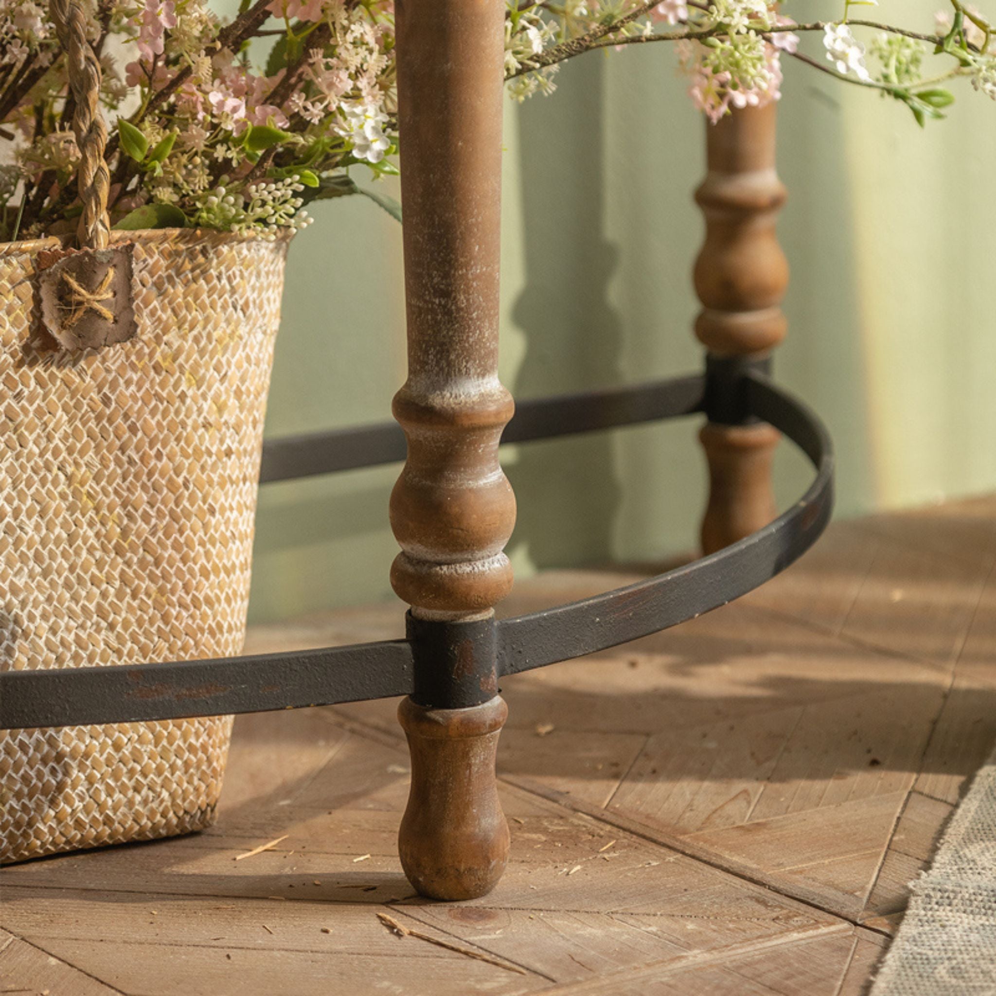 Floor-level detail of Clémence console, walnut turned leg meeting the black iron stretcher band at the base.