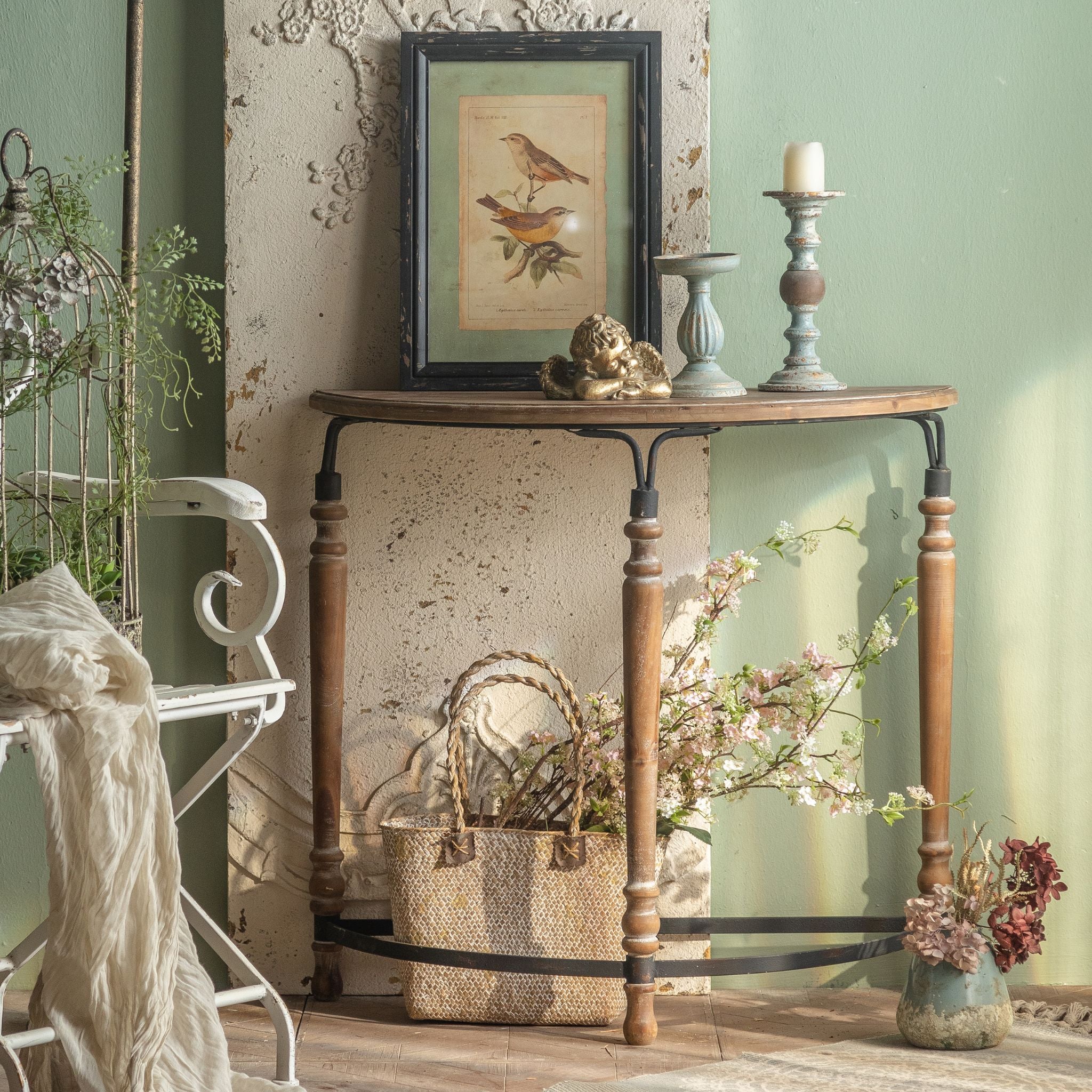 Clémence French Provincial half moon console table in walnut timber and black iron, styled in a French country alcove with botanical bird print, cherub, candlesticks and floral basket. Hero.