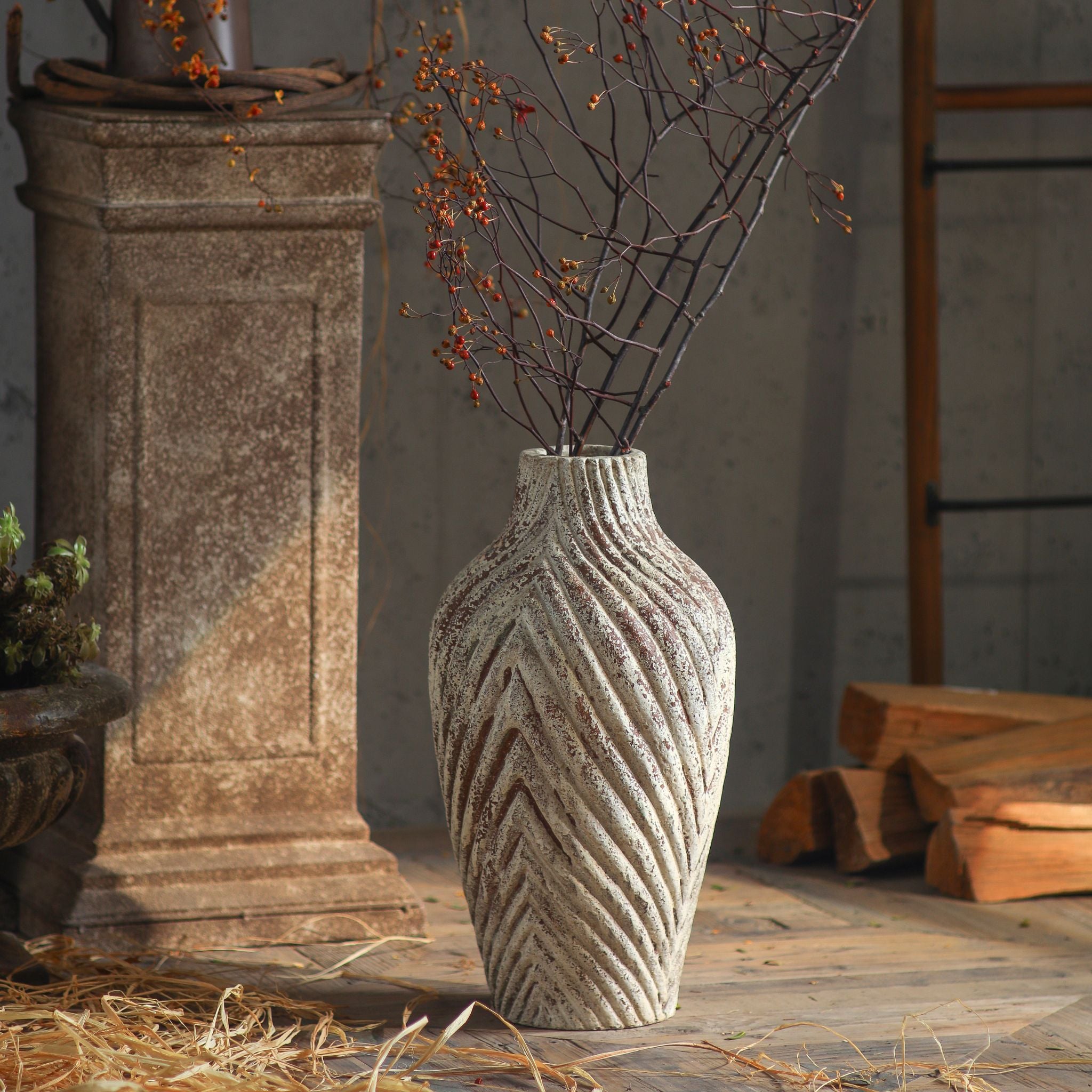 Clement chevron vase with branches in warm sunlight beside a stone pedestal