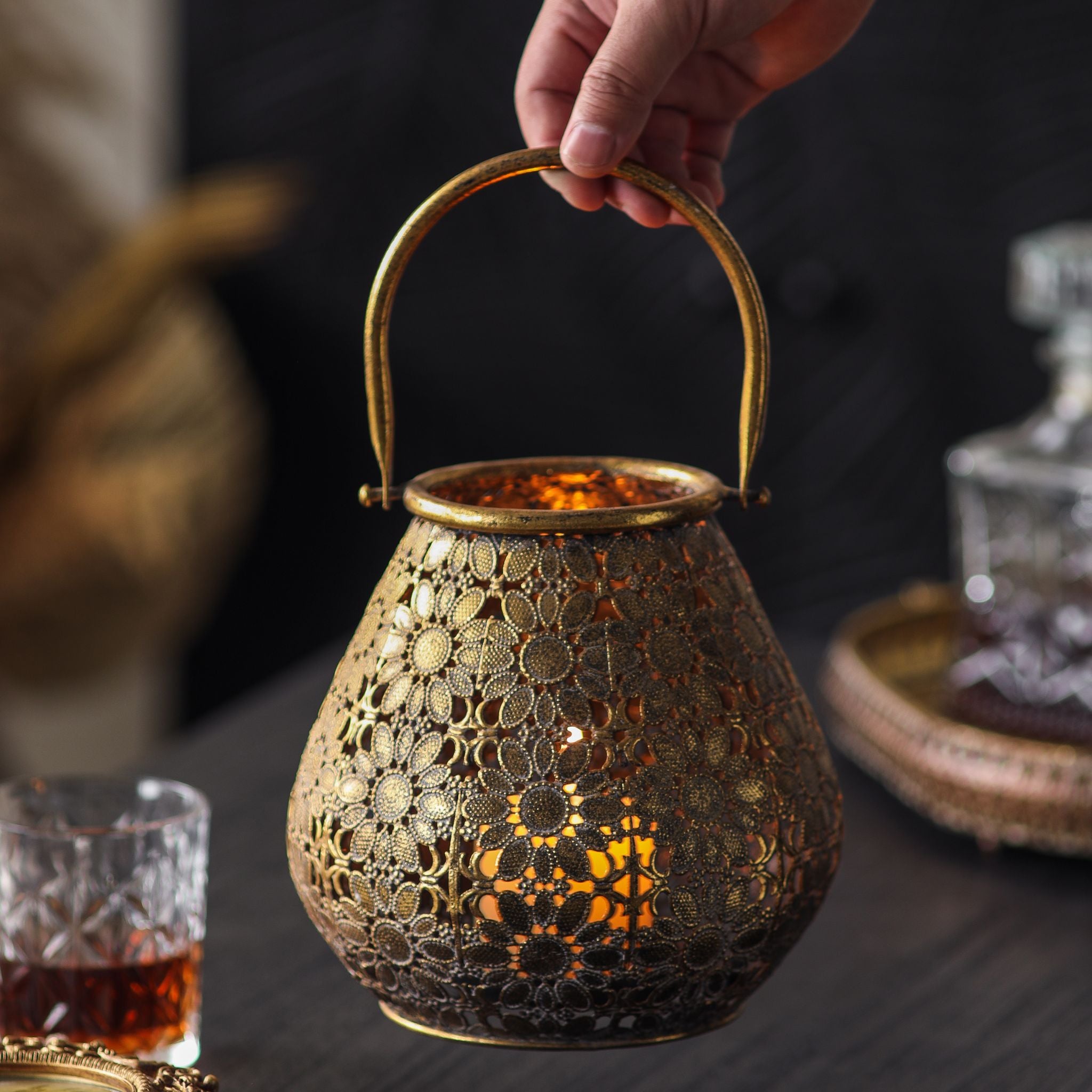 Lantern lifted by its arched antique gold handle, candlelight showing through the filigree