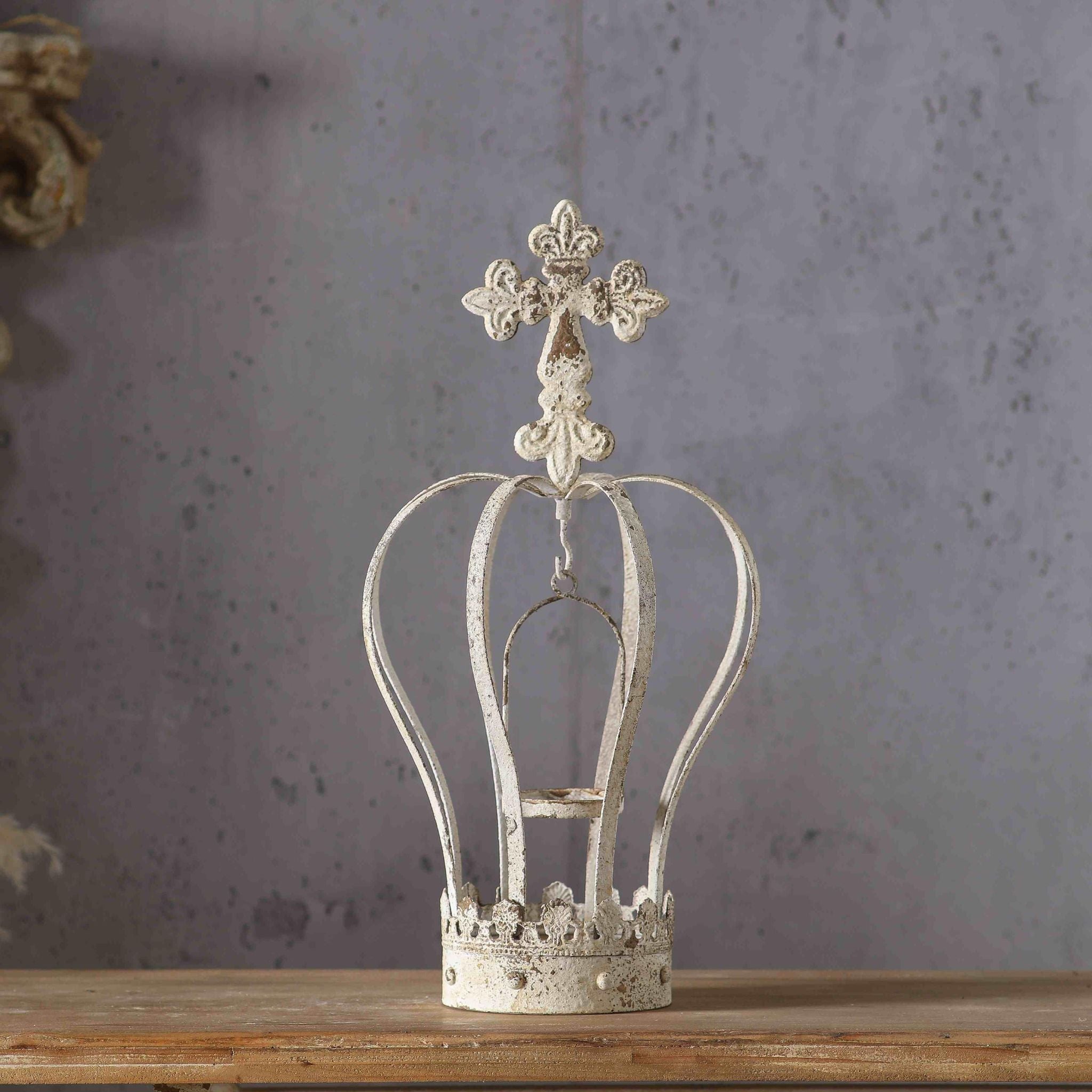 Blanche crown candle holder in distressed antique white metal with a cross finial, on a timber surface