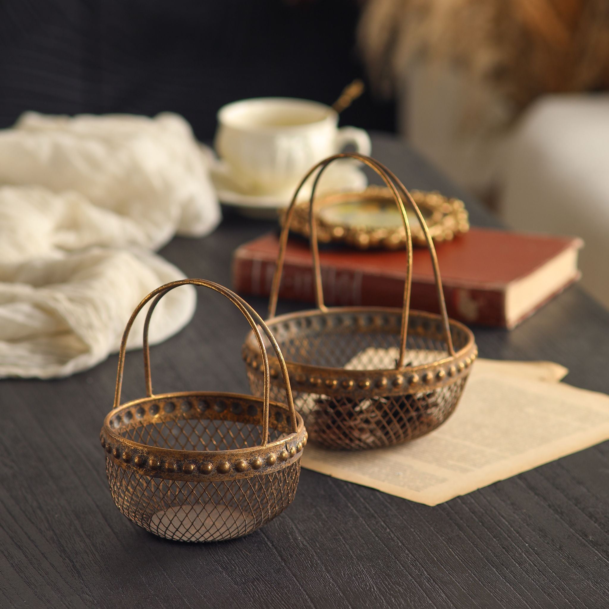 Diane French Provincial wire basket set of two in antique gold mesh, larger and smaller baskets with arched handles and beaded rims. Hero.