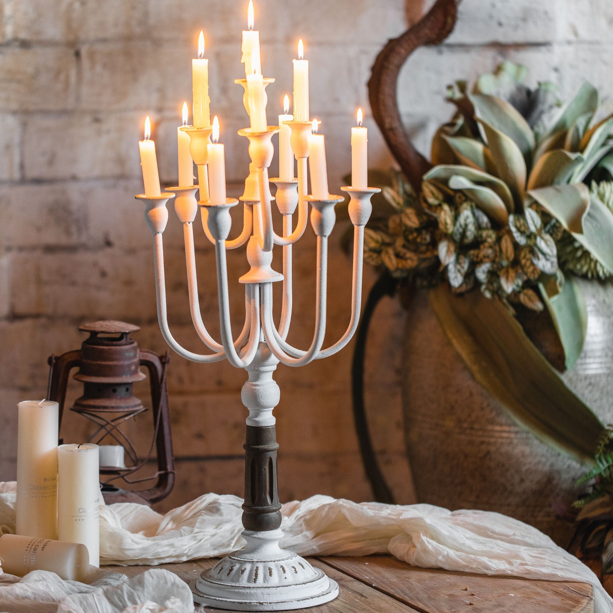 Étienne French Provincial twelve-arm candelabra in whitewashed iron with turned wood column, photographed lit with twelve burning taper candles, styled on a timber table with eucalyptus wreath and antique lantern. Hero.